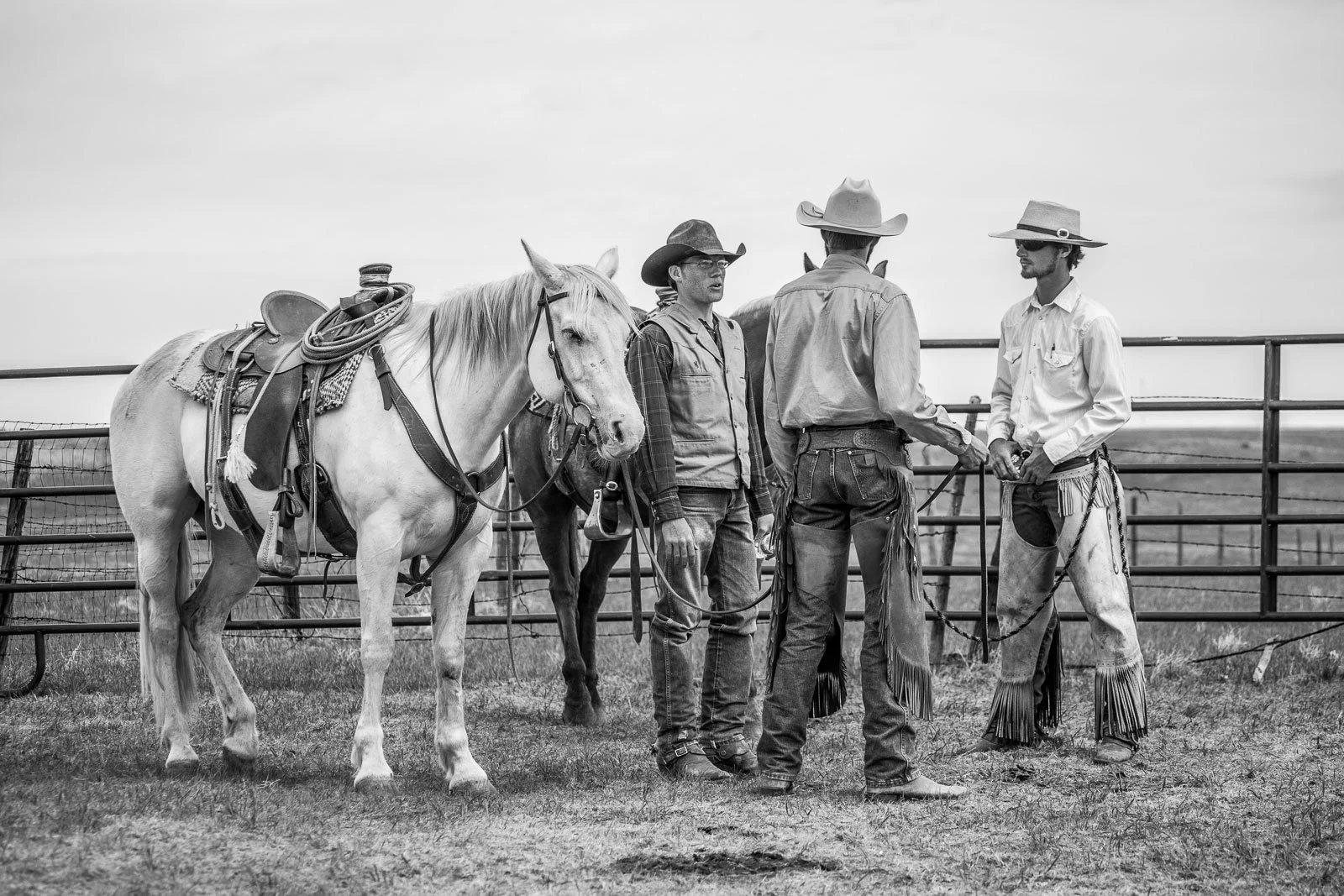 Black and white photo, cowboys talk at a ranch before a branding.