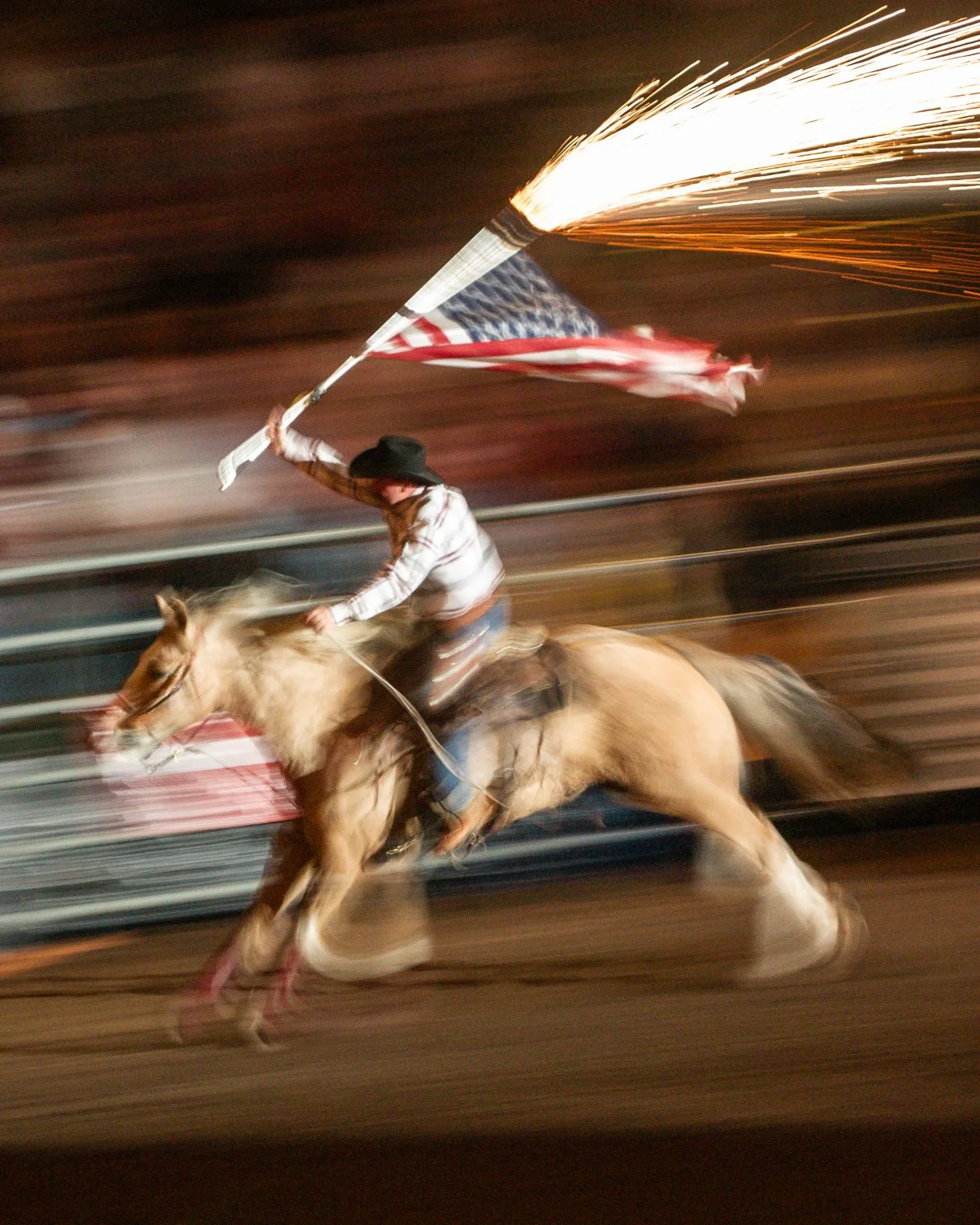 Cowboy carries a US Flag with fireworks during a grand entry at rodeo.