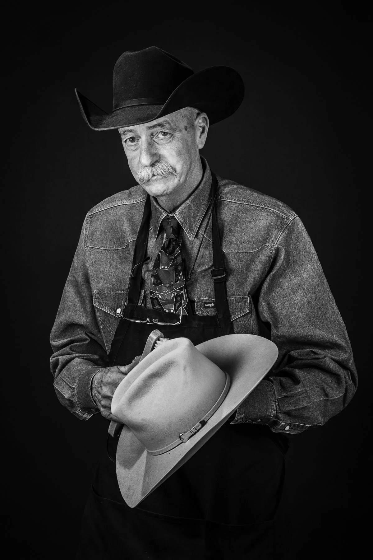 Black and white cowboy portrait for marketing for a hat maker. Cowboy cleaning a felt cowboy hat.