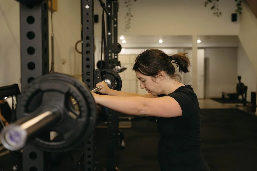 Woman preparing to lift weights in a toronto gym, standing next to a squat rack with weights.
