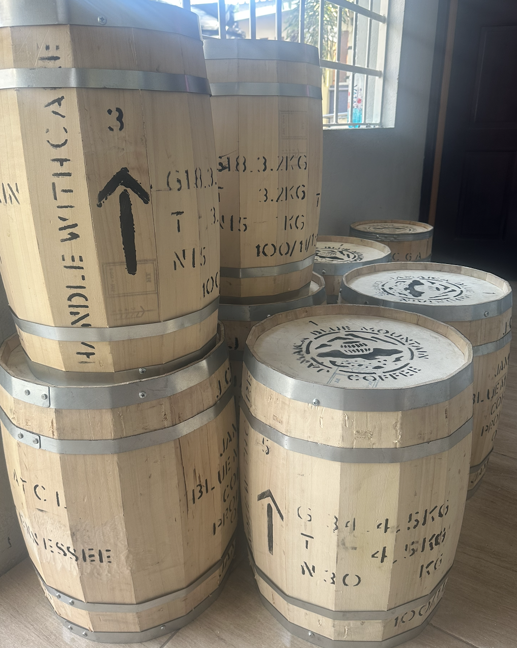 Several wooden barrels with black markings and arrows on the surface, arranged indoors near a window and a dark cabinet.