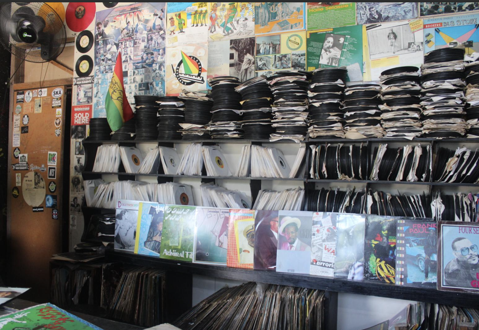 A music store filled with shelves of vinyl records and CDs, with a graffiti-style mural, posters, and flyers on the wall, and a small flag in the corner.