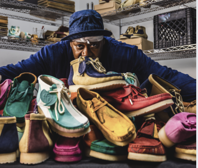 A person wearing a blue hat and jacket inspecting a pile of colorful shoes on a table in a storage or warehouse space.