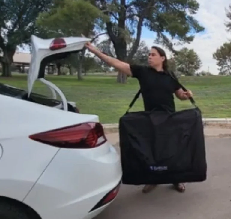 This picture displays an image of a professional massage therapist carrying a mobile massage table to be use in the convenience of client's home. The image clearly instructs to please call 520-339-3972 to discuss scheduling and pricing details.  