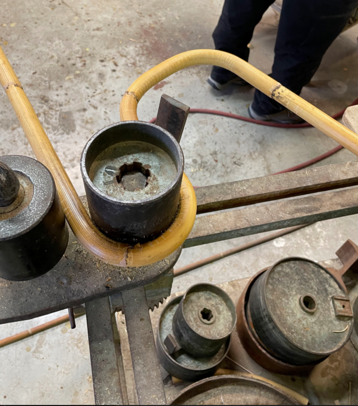 Machine de forge avec différentes pièces en métal et tuyaux en bambou, dans un atelier de soudure.