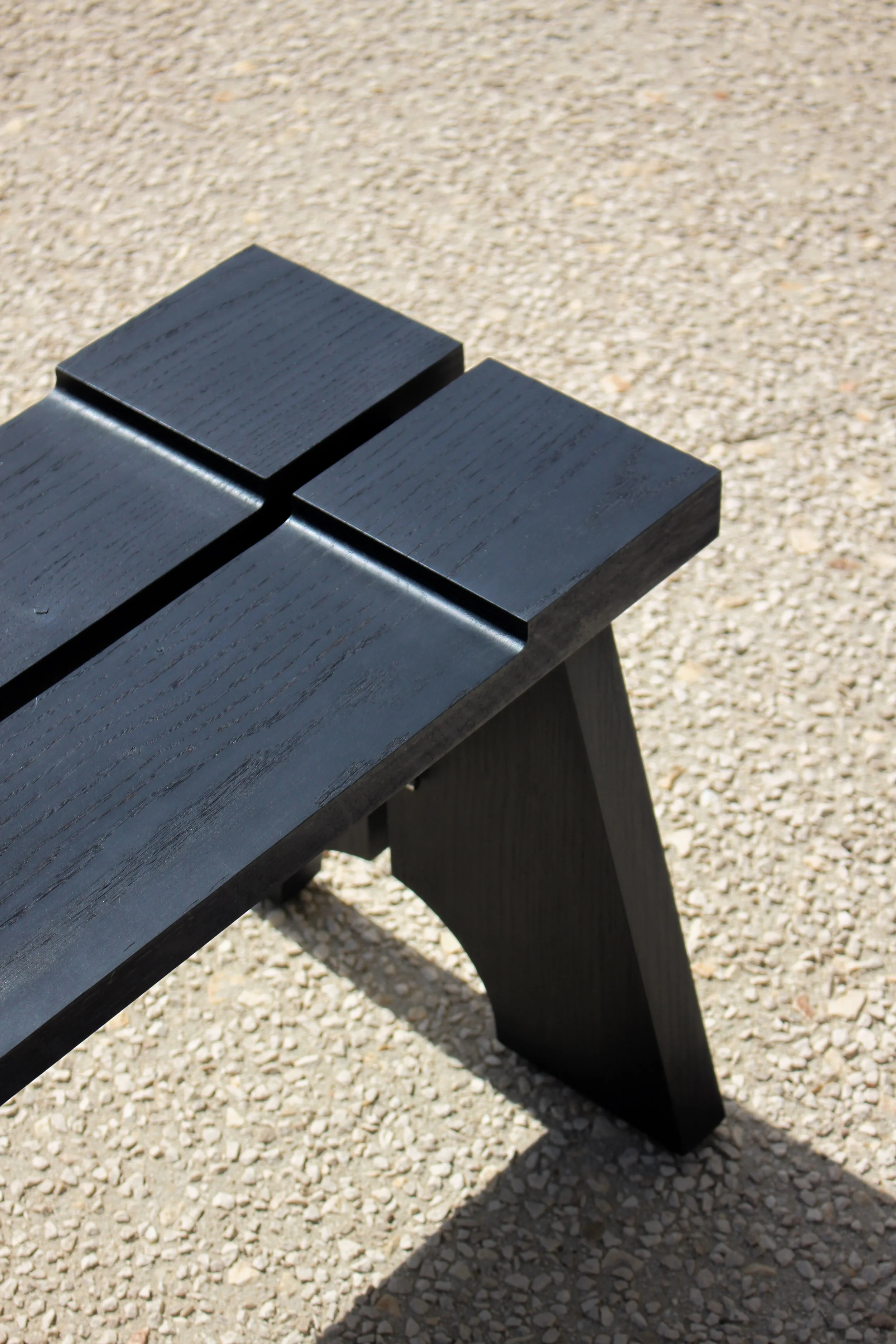 Un banc en bois noir placé sur un sol en gravier.