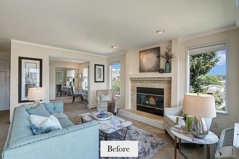 Living room with blue sofa, armchair, fireplace, wall art, and window showing a view of trees and sky.