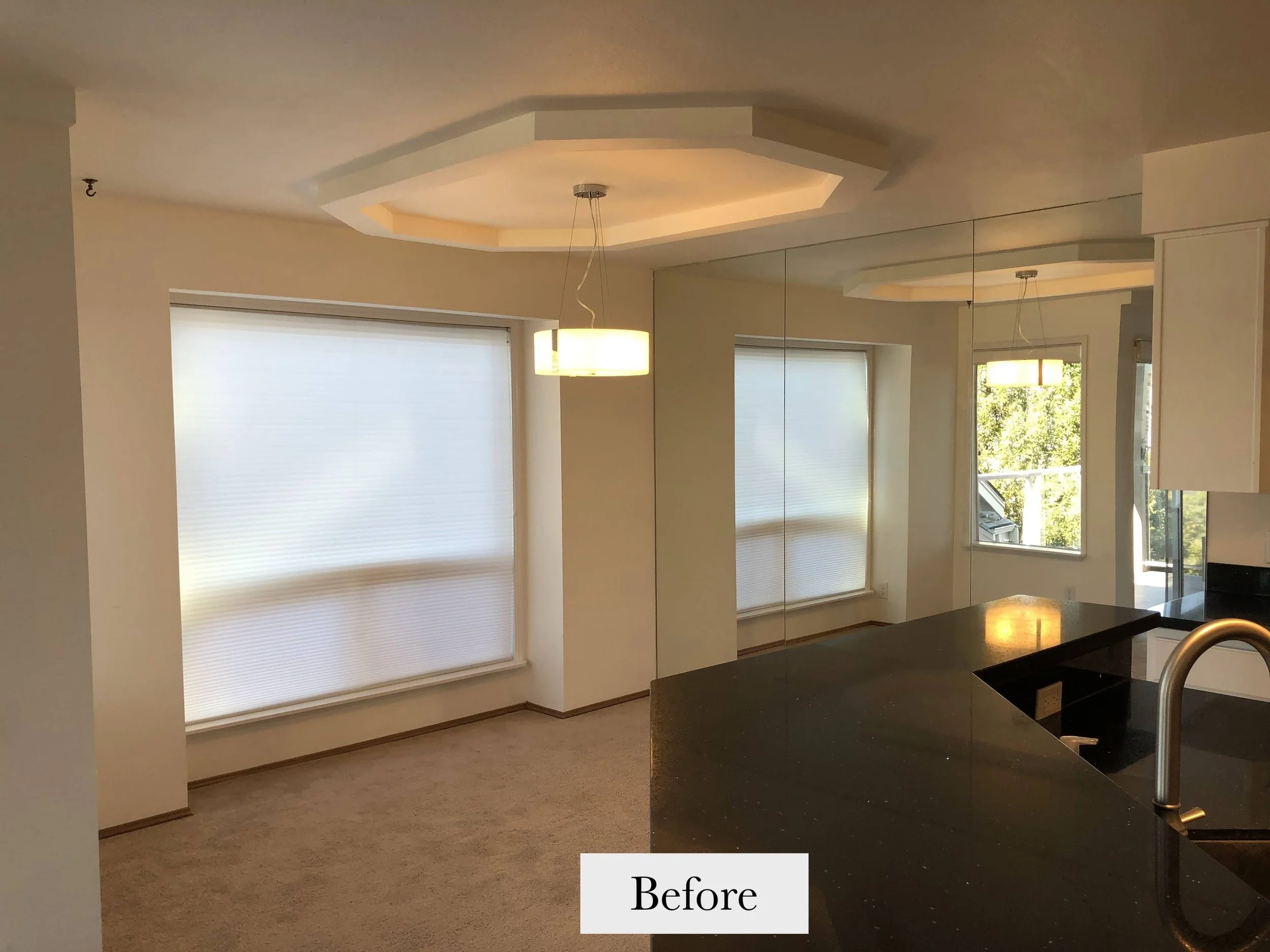 Empty living room with large windows and a kitchen island in the foreground.