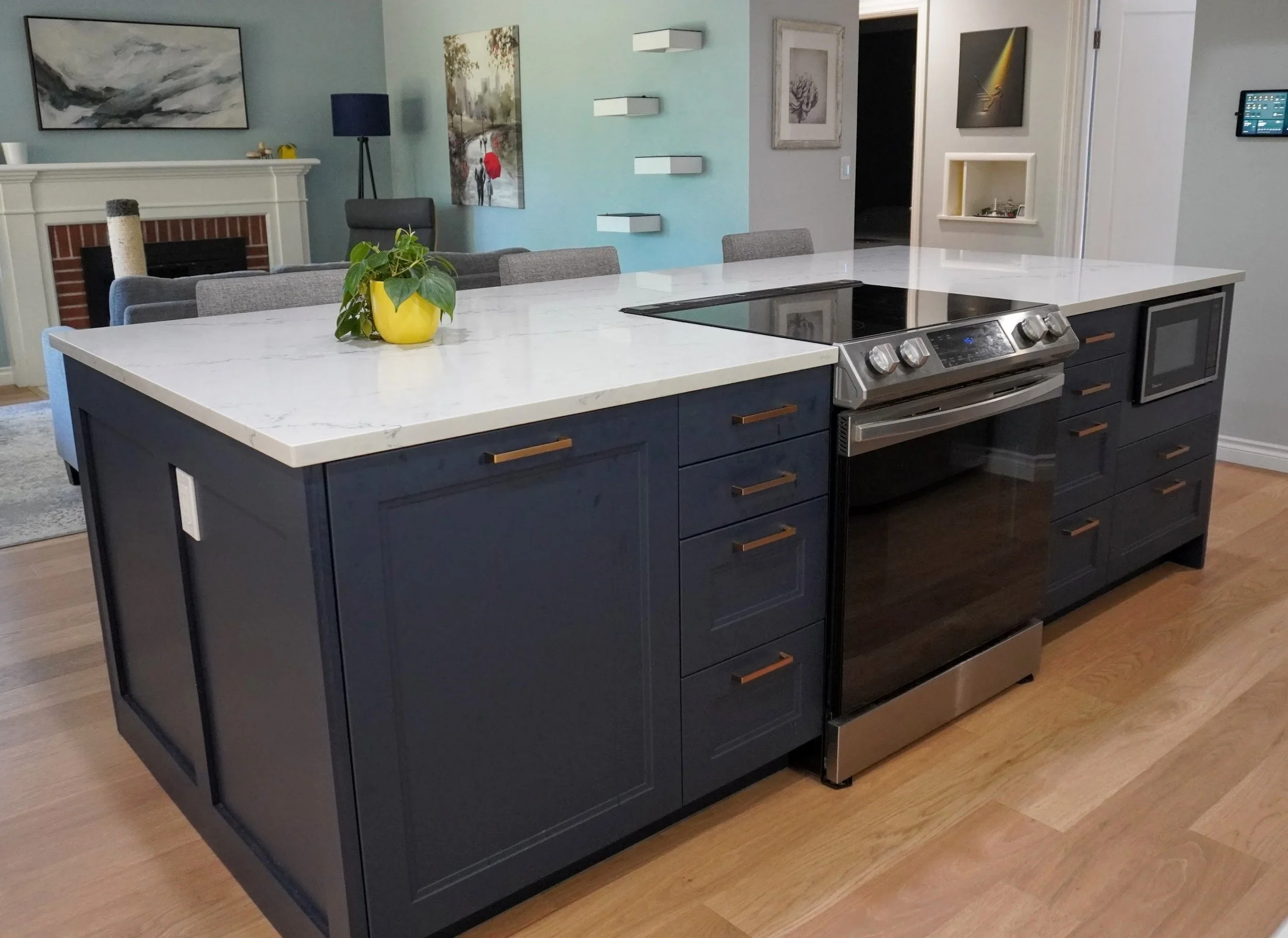 Modern kitchen island with a dark blue base, white marble countertop, built-in stove, microwave, and a yellow potted plant on top.