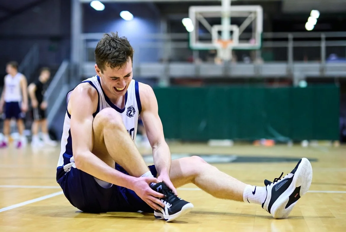 Injured basketball player holding his ankle on the court after landing awkwardly
