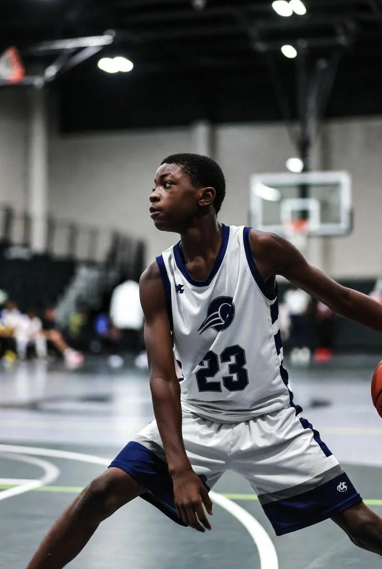 Youth basketball player in defensive stance during game on indoor court