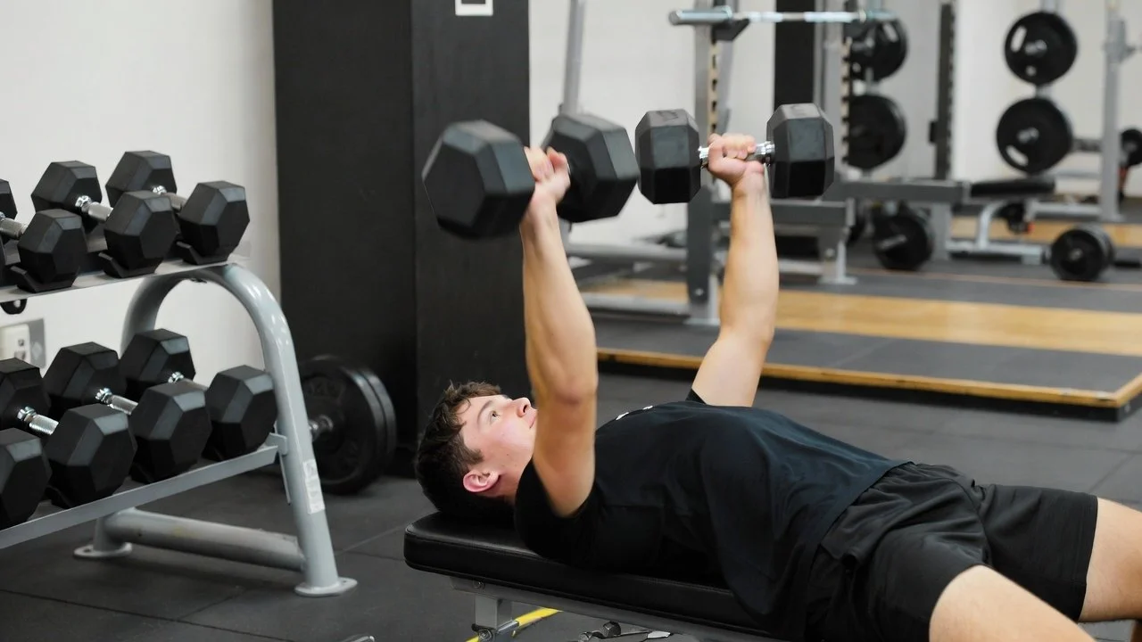 Basketball player performing dumbbell bench press as part of a basketball weight training program