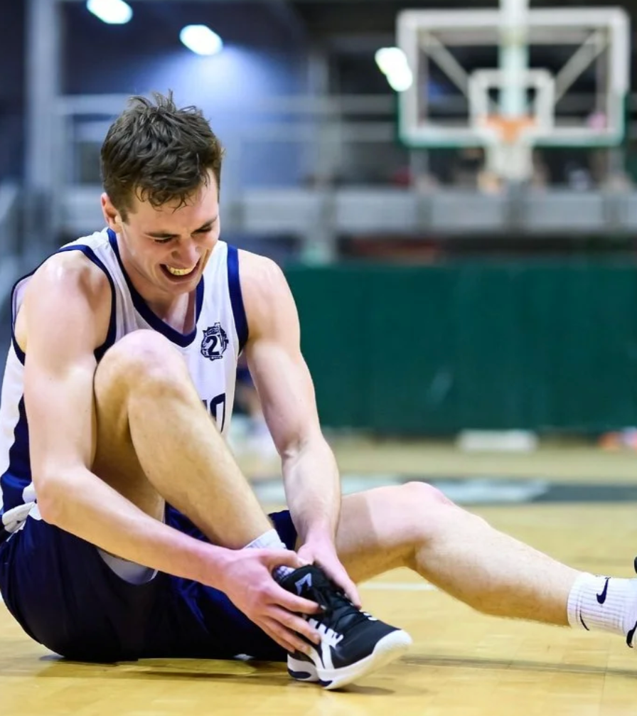 Basketball player holding ankle in pain after injury on the court during a game