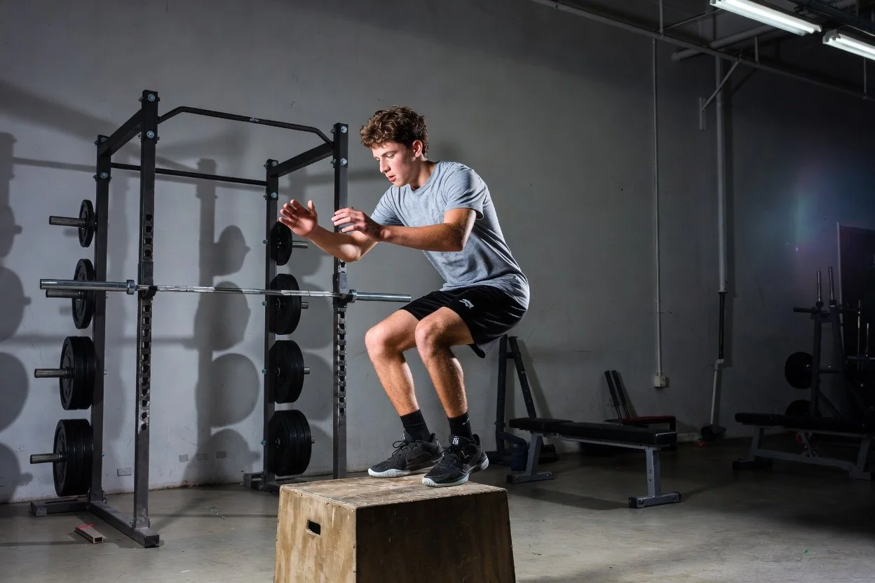 basketball player practicing box jump landing mechanics in gym