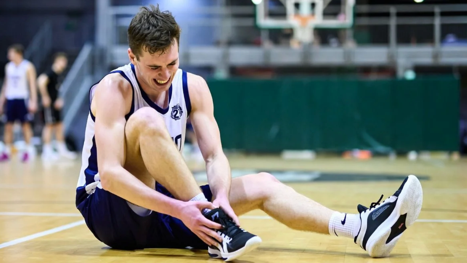 basketball player sitting on court holding ankle after injury
