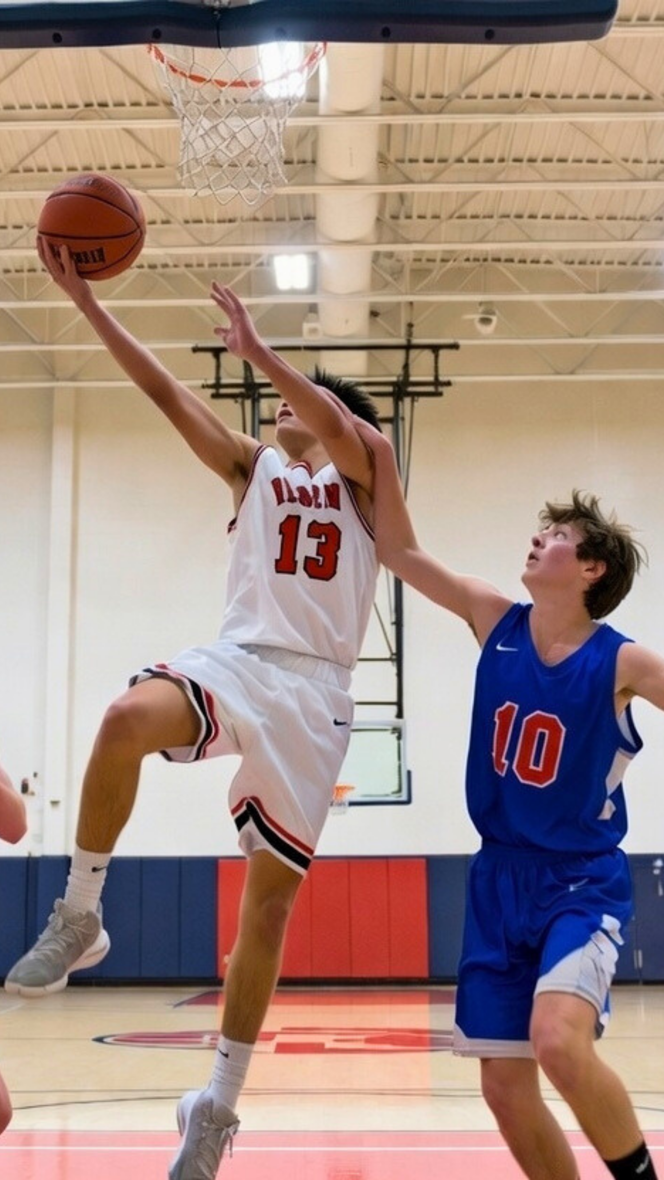 High school basketball player performing a layup under defensive pressure, highlighting landing mechanics and injury risk