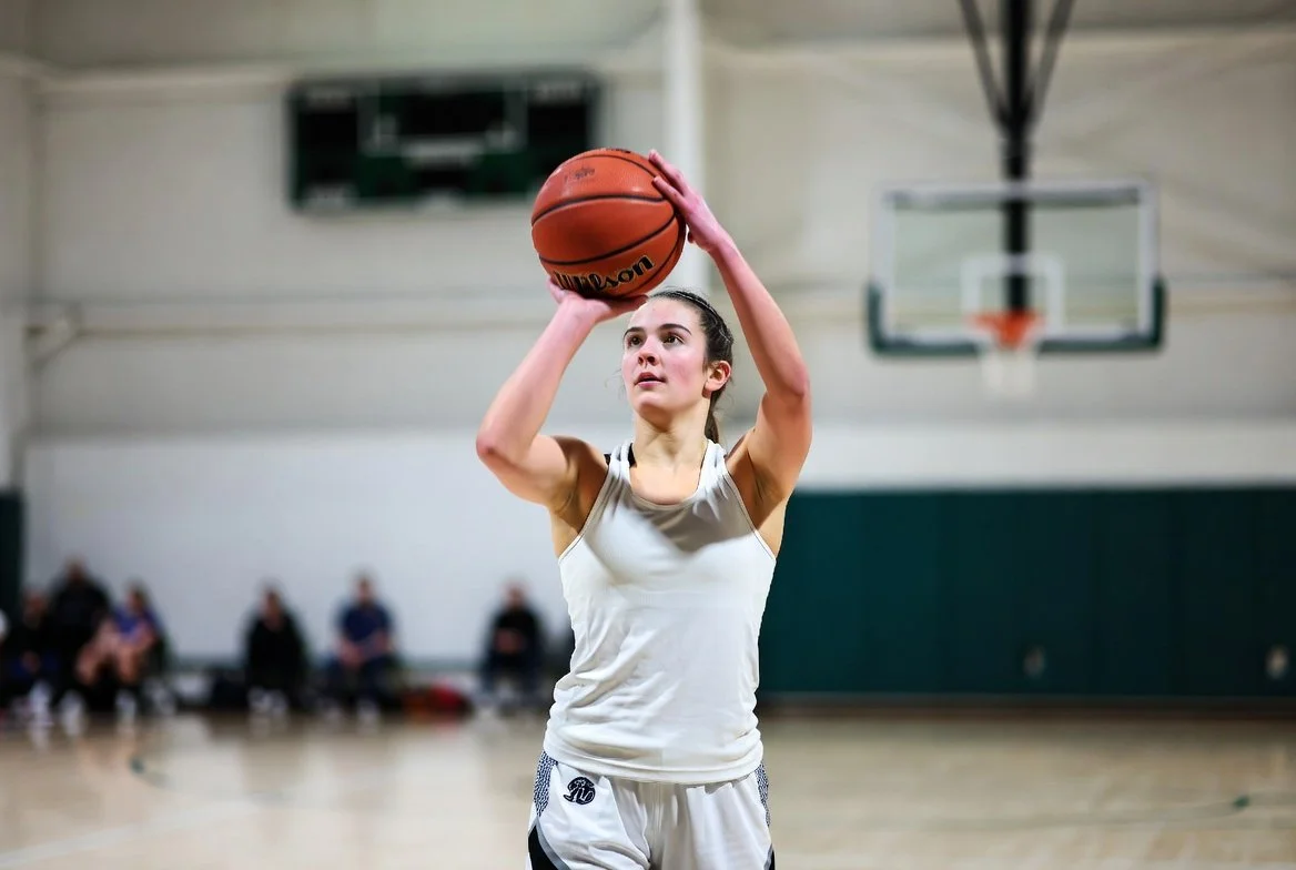Female basketball player shooting a jump shot during an indoor game while focusing on proper shooting form and balance