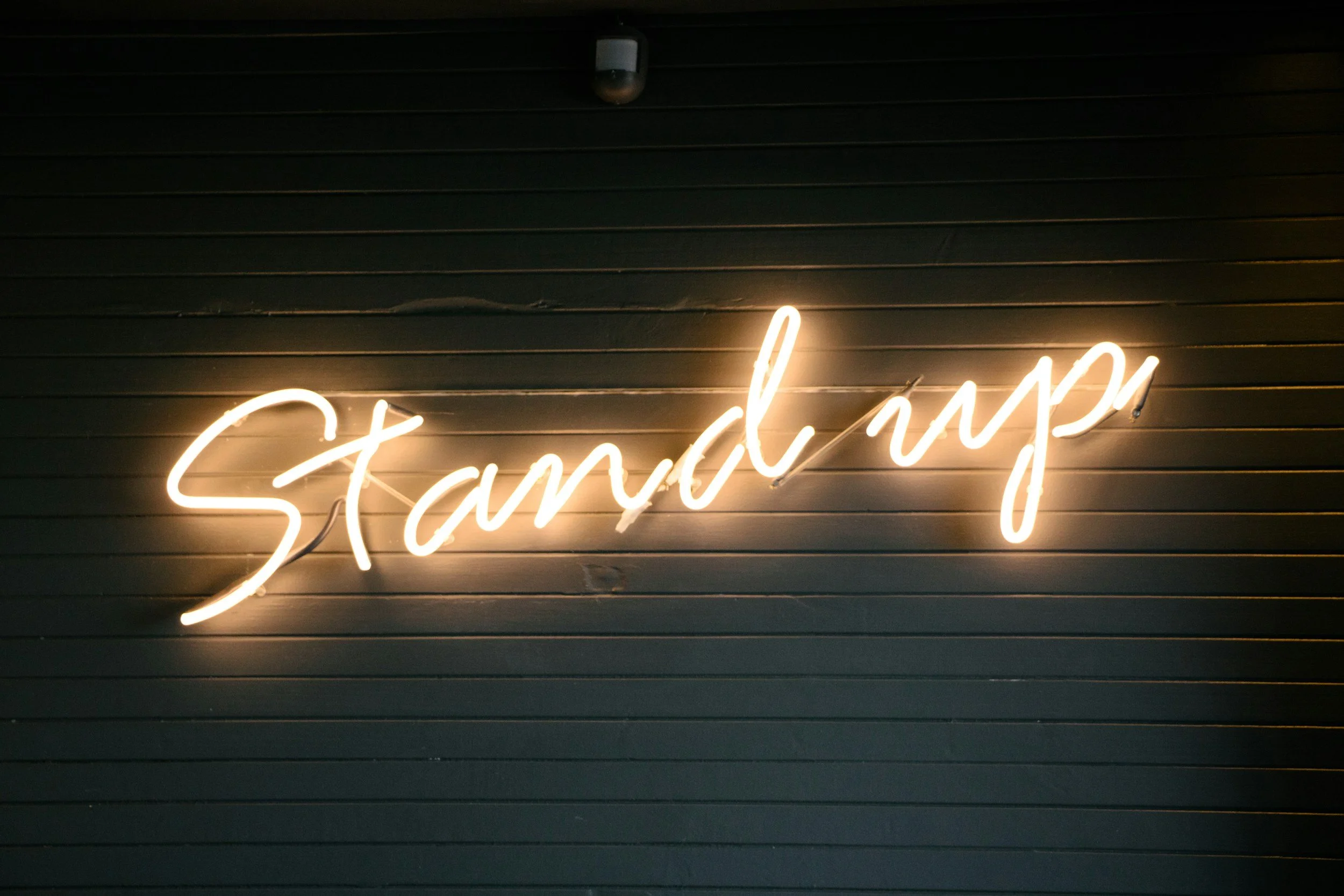 Neon sign reading 'Standing' mounted on a dark wooden wall.