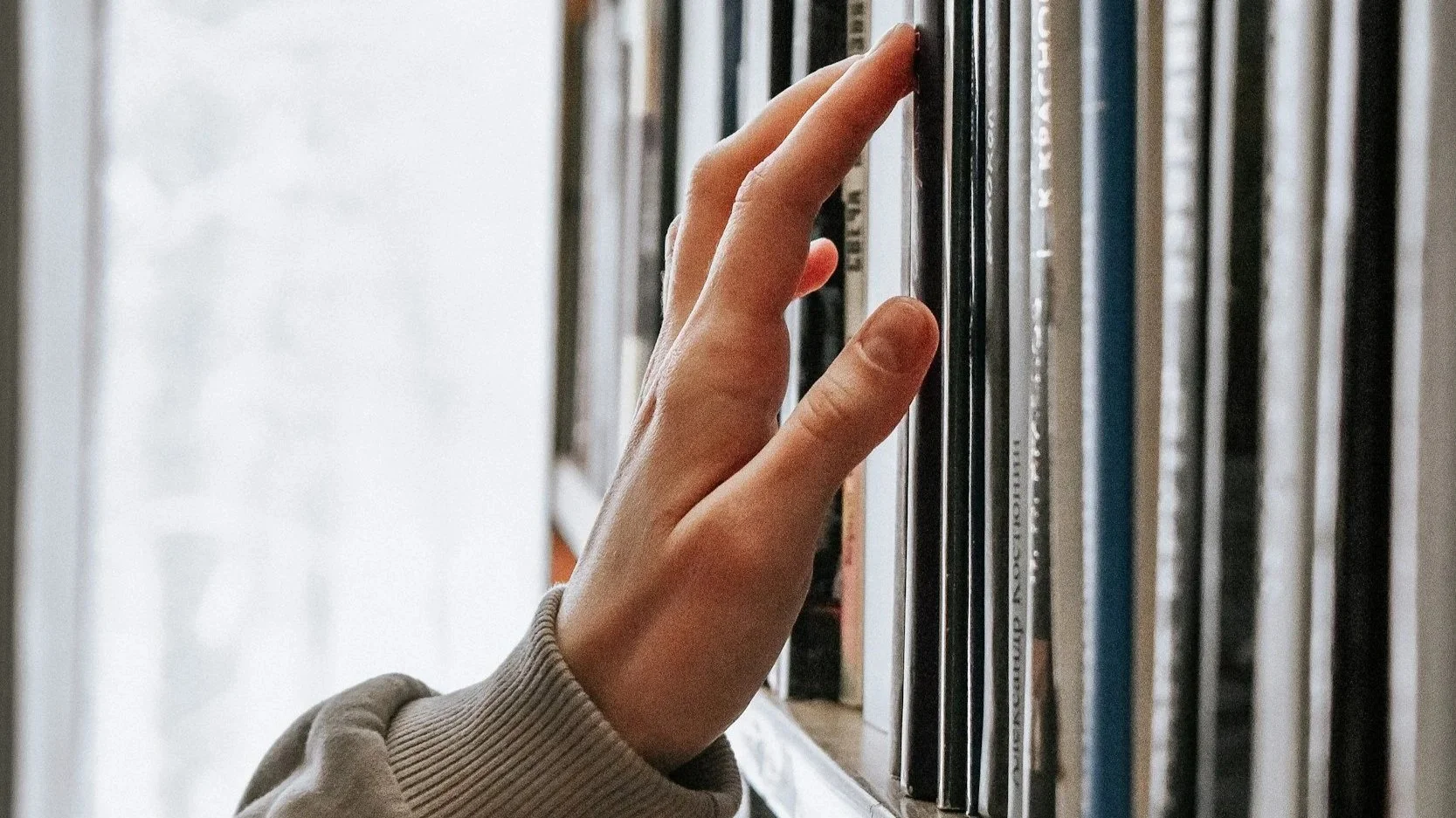 A hand reaching out to select a vinyl record from a shelf filled with other records.