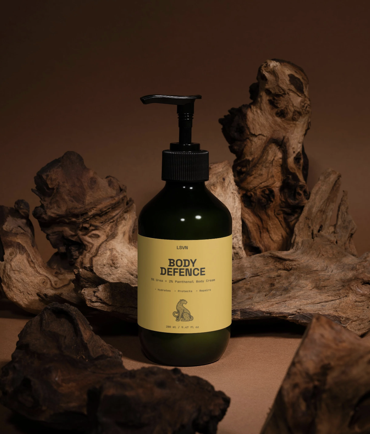 A black pump bottle labeled 'Body Defence' with a yellow label, surrounded by pieces of driftwood on a brown background.