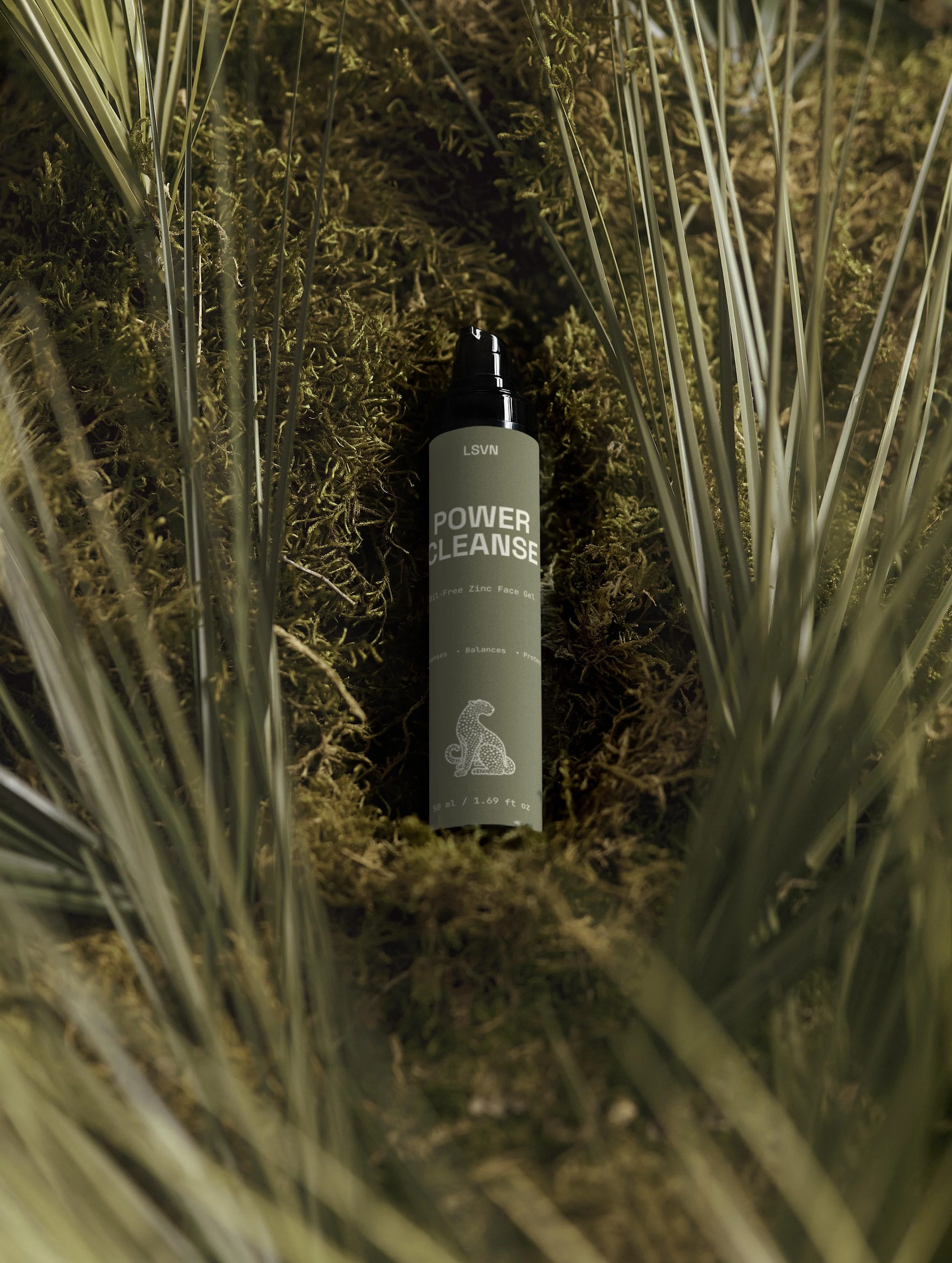 A bottle labeled 'Power Cleanse' lying in a small patch of moss surrounded by tall green grass.