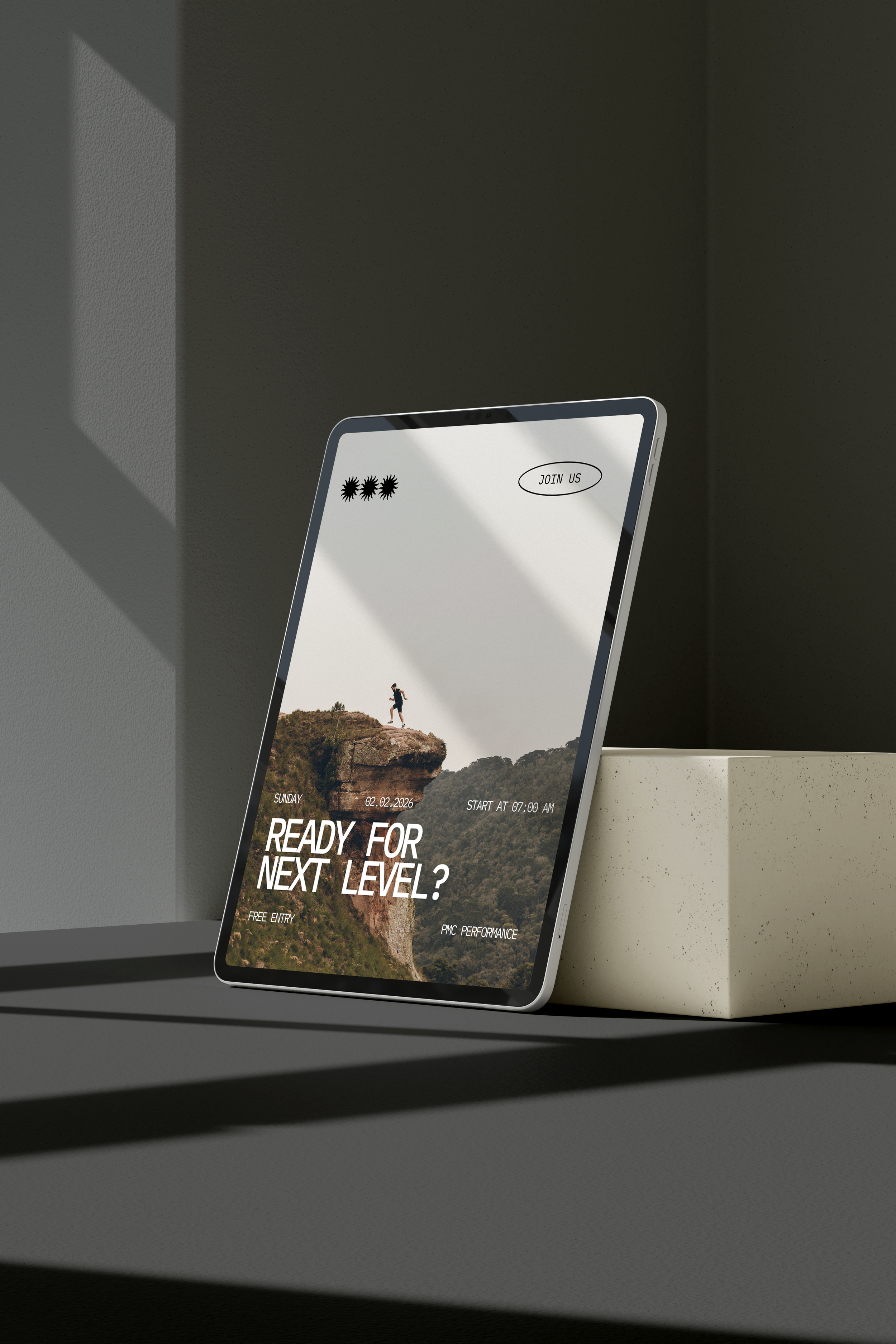 A tablet displaying promotional content for an outdoor adventure event, with photo of a hiker on a cliff, event details, and a 'Join Us' button, placed on a light-colored block on a gray surface with shadows from window blinds.