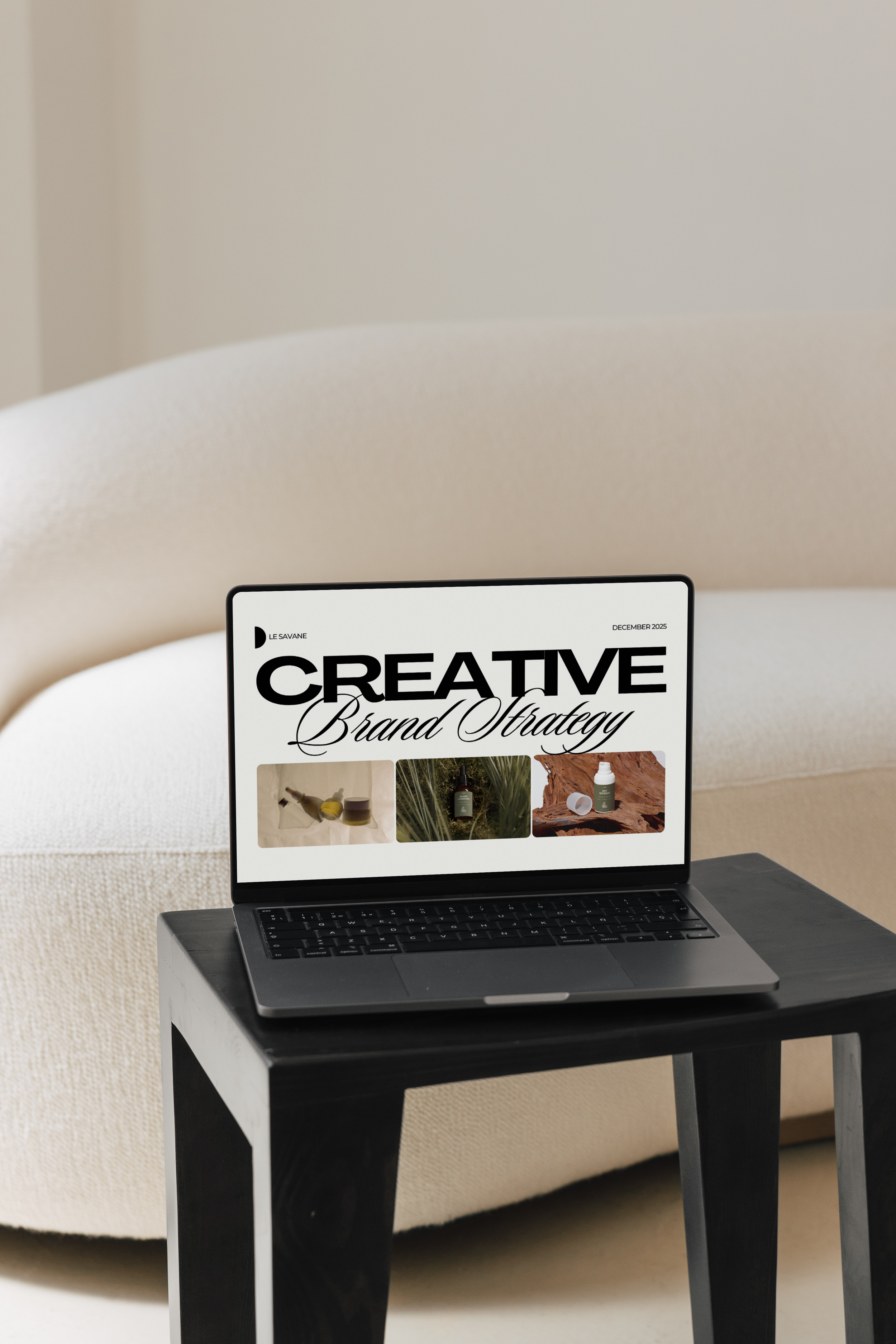 A laptop displaying a magazine cover titled 'Creative Brand Strategy' with three images of products and nature scenes on a black side table in front of a beige sofa