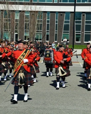 A parade with a marching band in red uniforms, playing instruments on a street near a modern glass building.