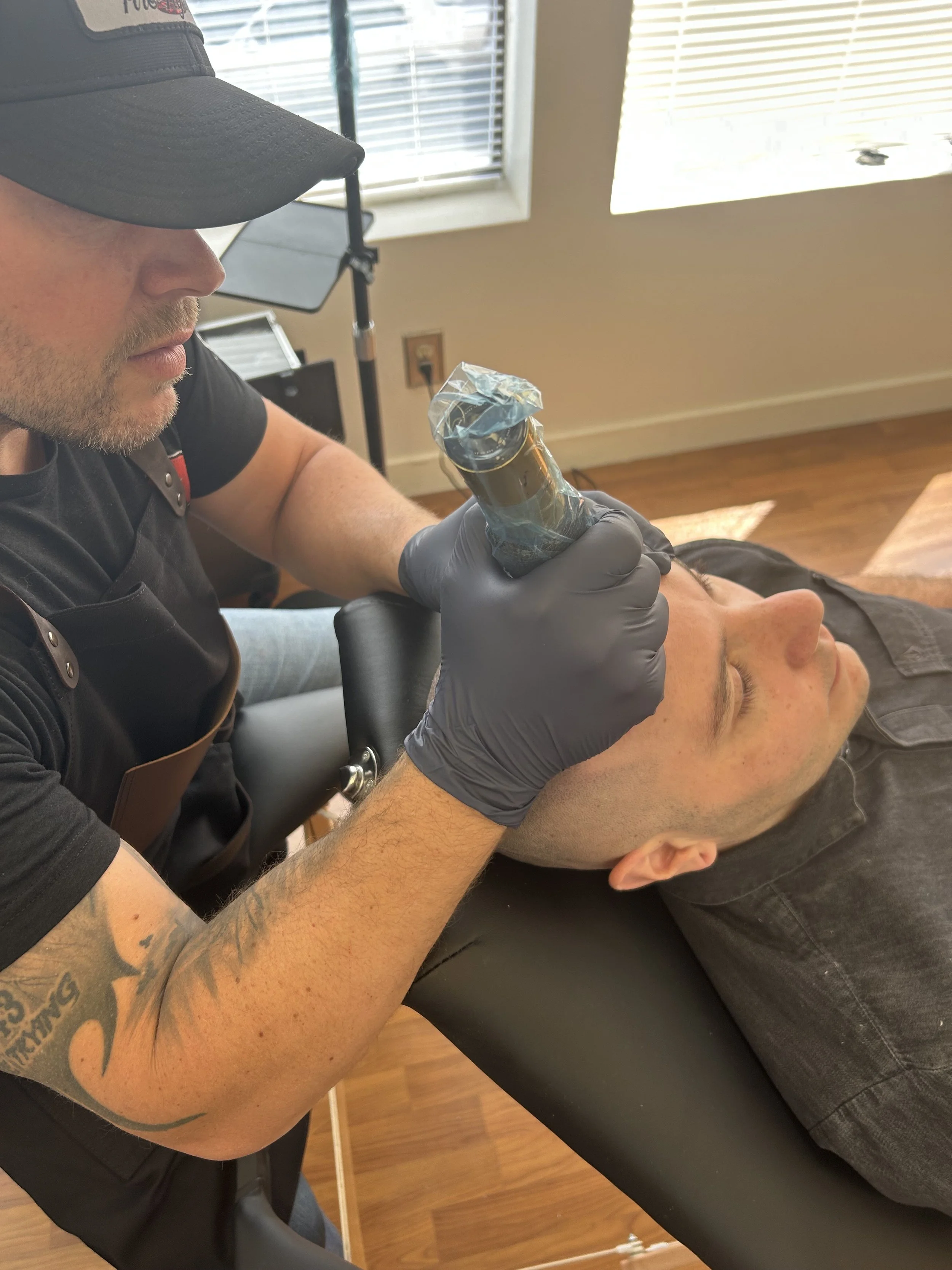 Tattoo artist working on a man's face with a tattoo machine in a tattoo studio.