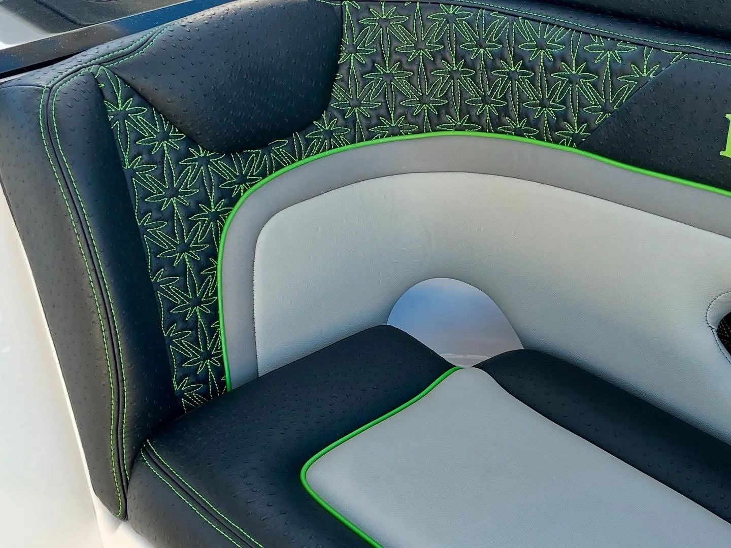 Close-up of a modern boat seat with navy blue, light gray, and green piping, featuring a pattern of green marijuana leaf outlines on the backrest.