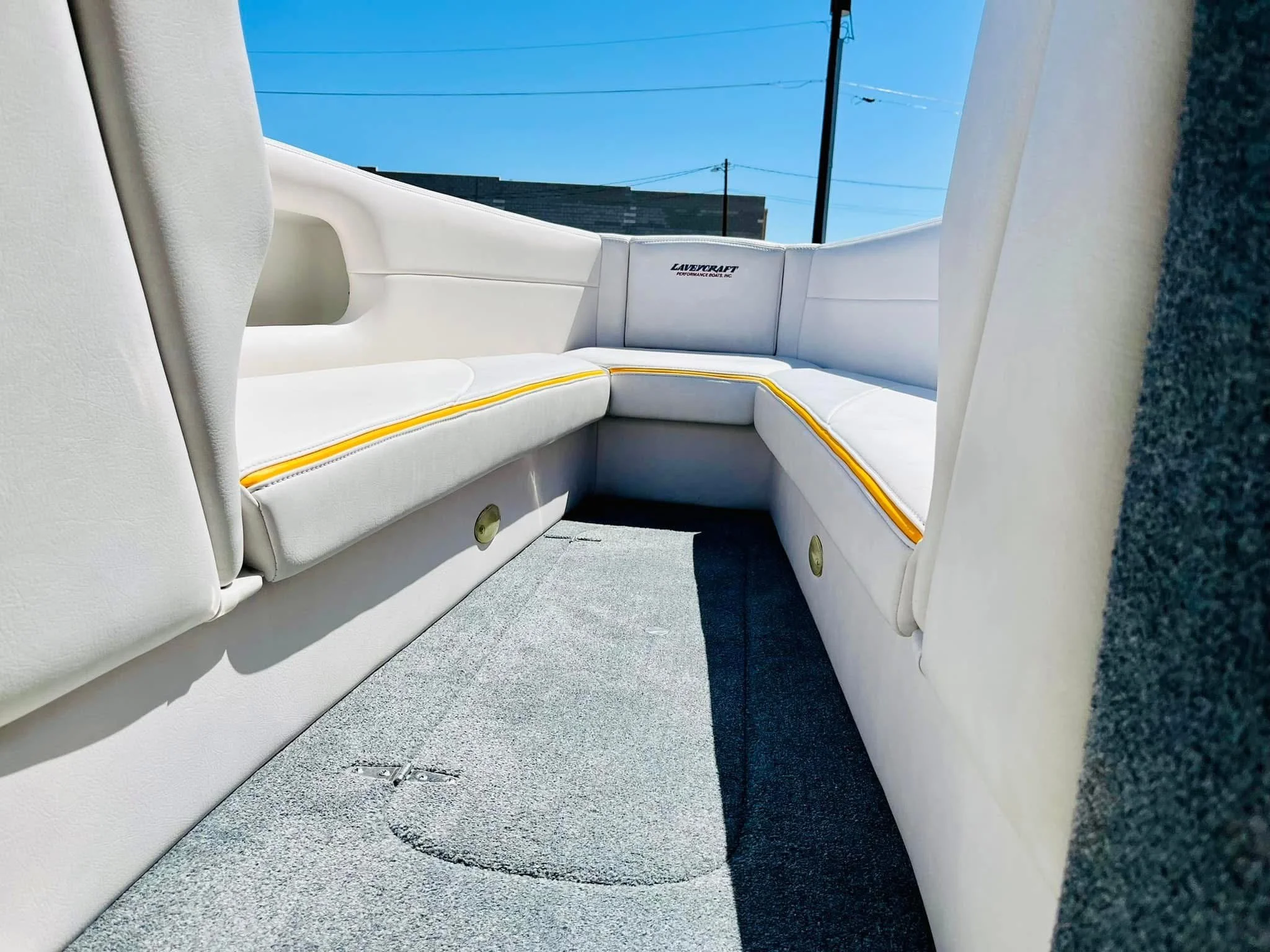 Inside of a boat with white cushioned seating around the perimeter, a gray carpeted floor, and a clear blue sky outside.