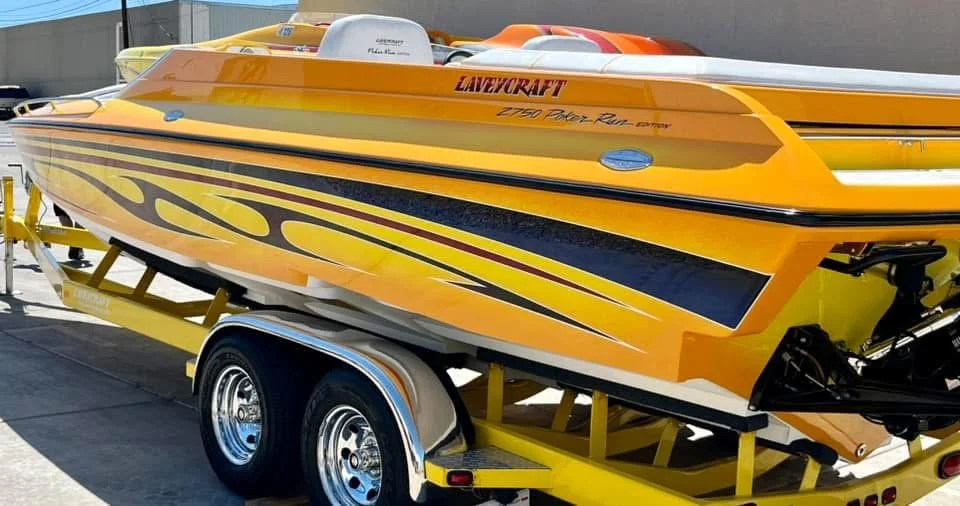 Bright yellow race boat mounted on a trailer at a boat dealership or storage yard.