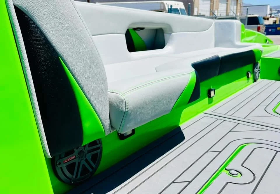 Close-up of a boat's seating with a light gray cushion and a built-in speaker at the base, featuring bright green accents and a black speaker grille.