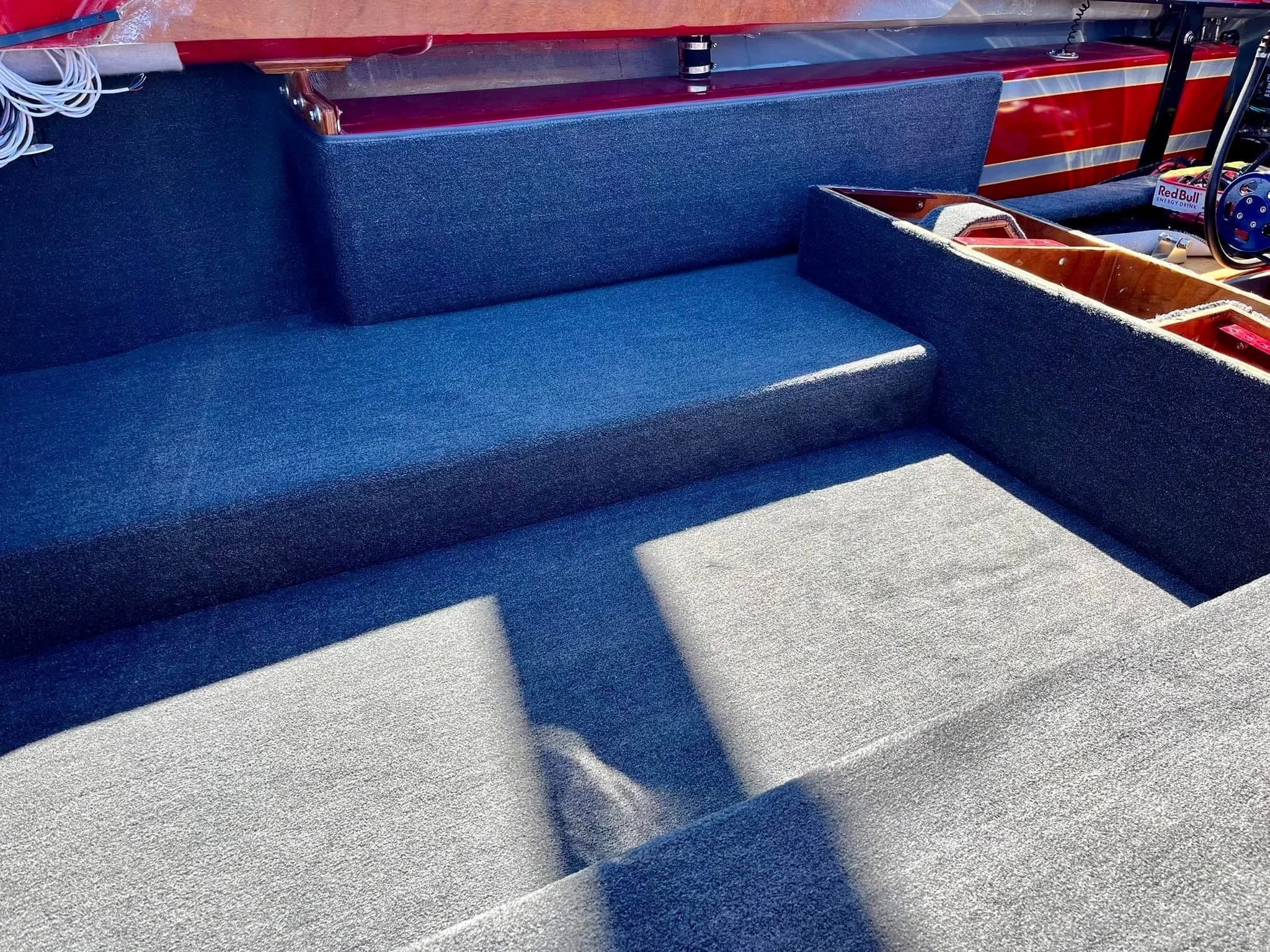 Interior of a boat with navy blue upholstery and gray carpet, showing seating and storage compartments.