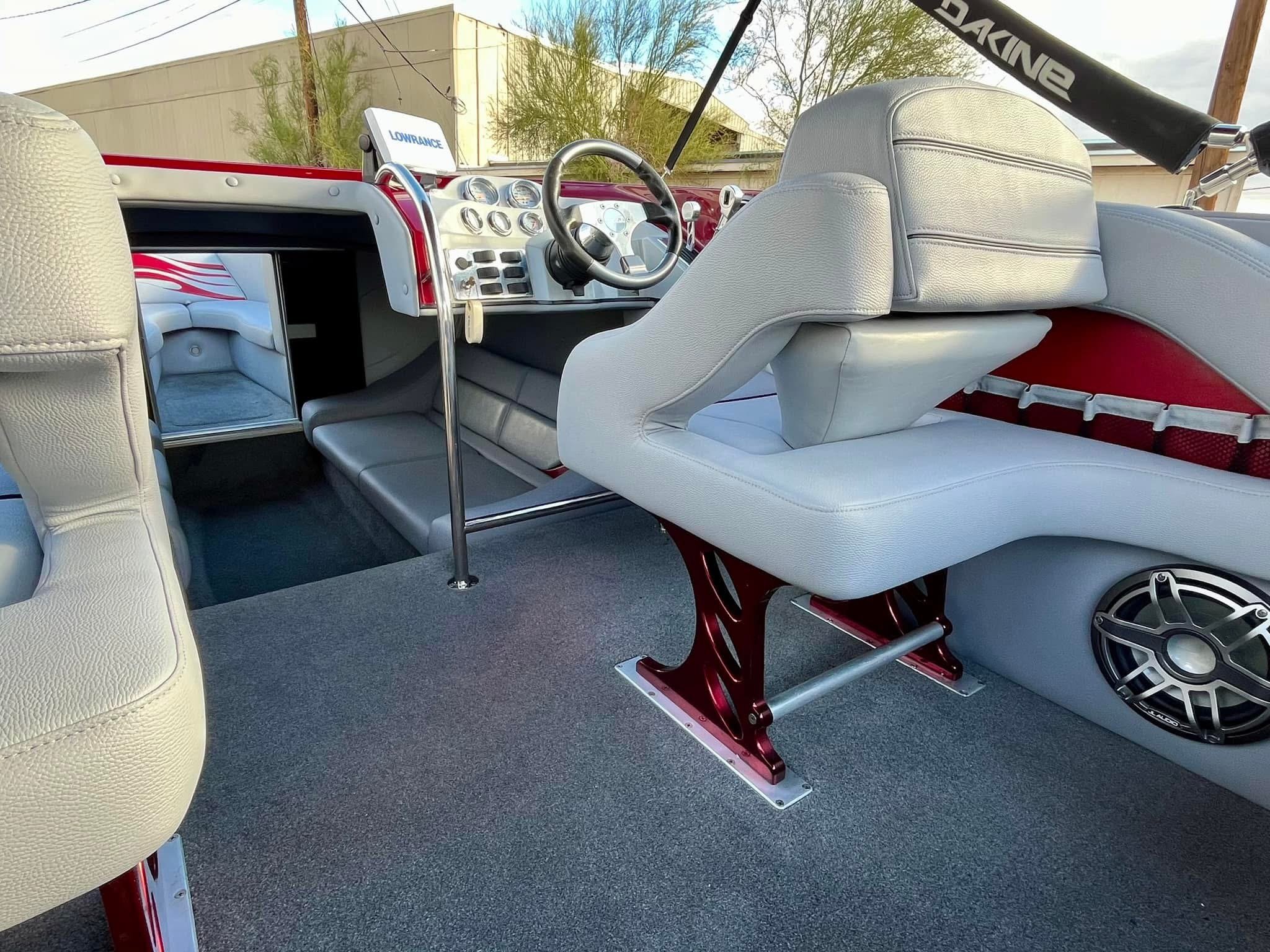 Interior of a boat showing white seating, a steering wheel, and a dashboard with gauges and equipment, with a speaker mounted on the side.