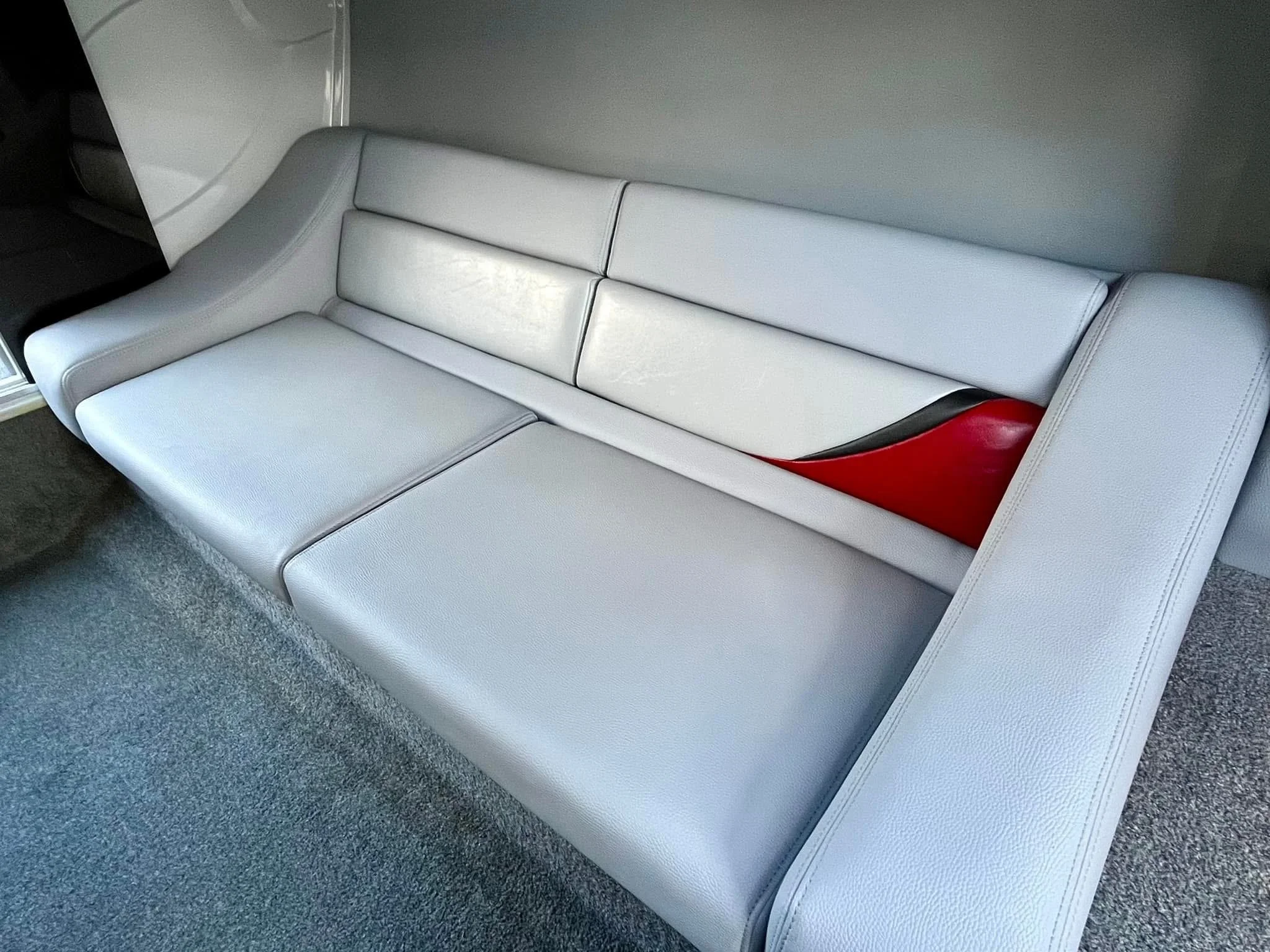 A light gray sectional sofa with a sleek modern design, placed against a wall with a small red and black accent detail on the backrest.