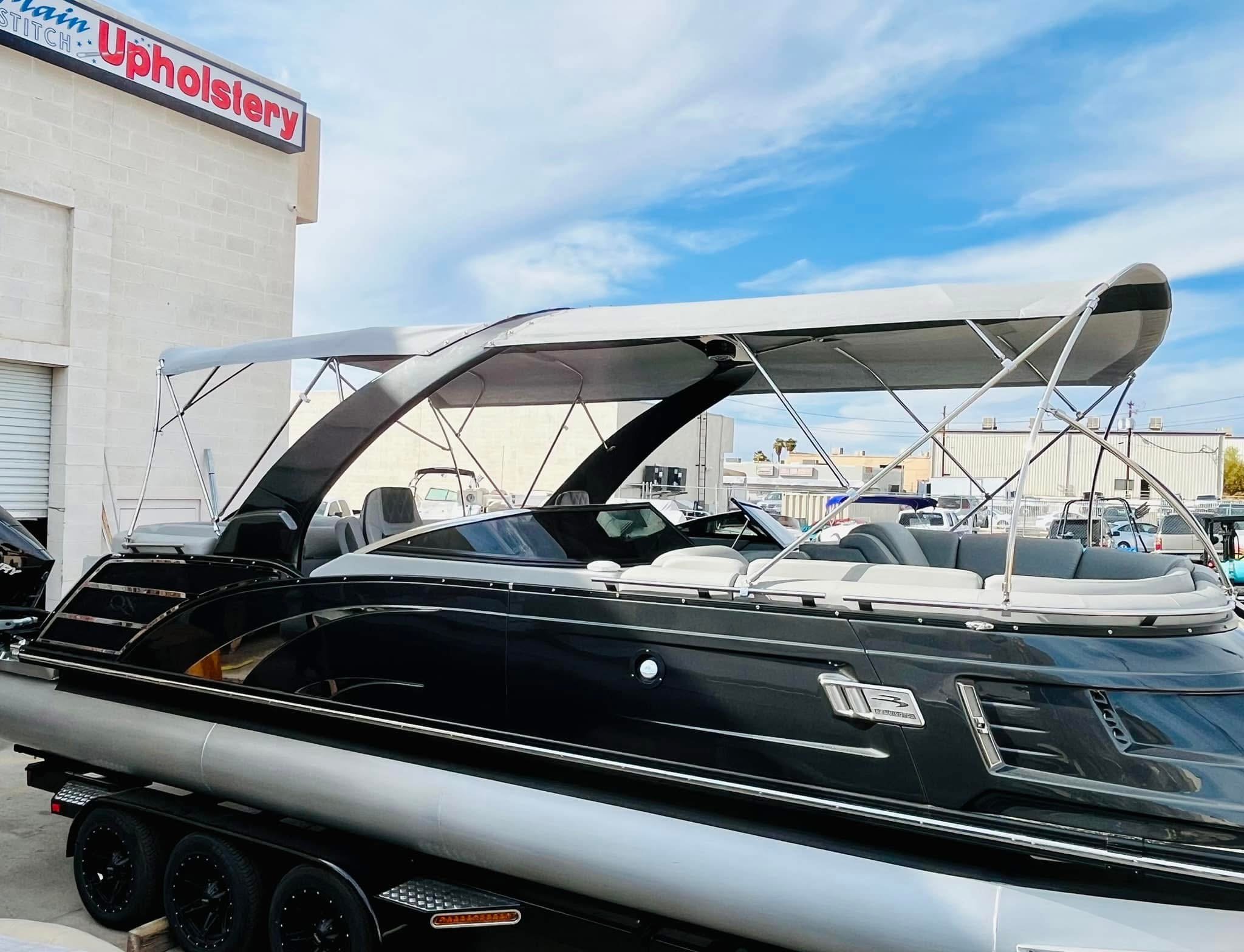 A black and silver luxury yacht with a canopy, on a trailer near an upholstery store, on a partly cloudy day.