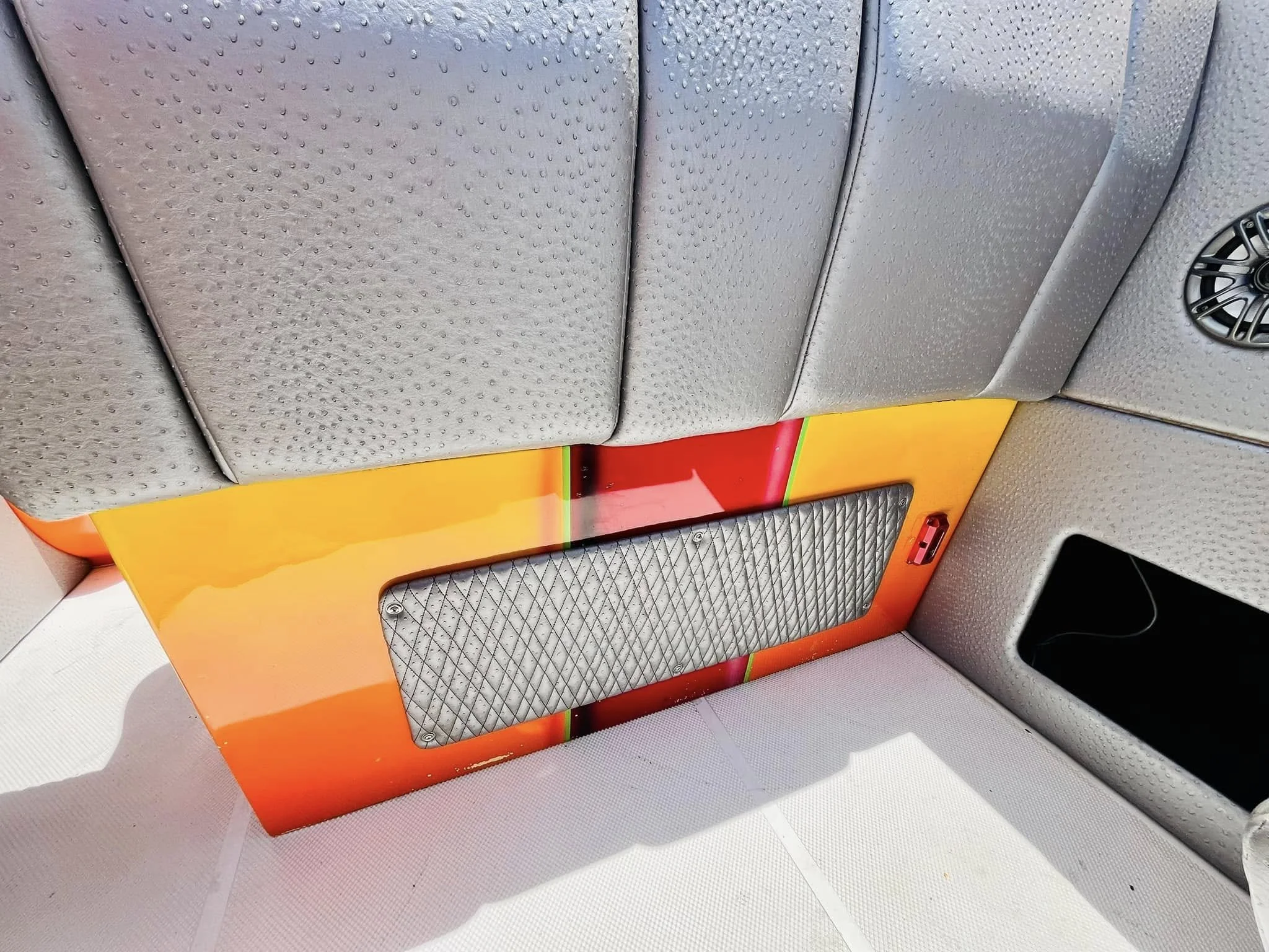 View of the interior of a vehicle, showing upholstered seats, part of a red, orange, yellow, and green painted panel, a gray patterned vent, and a black speaker grille.