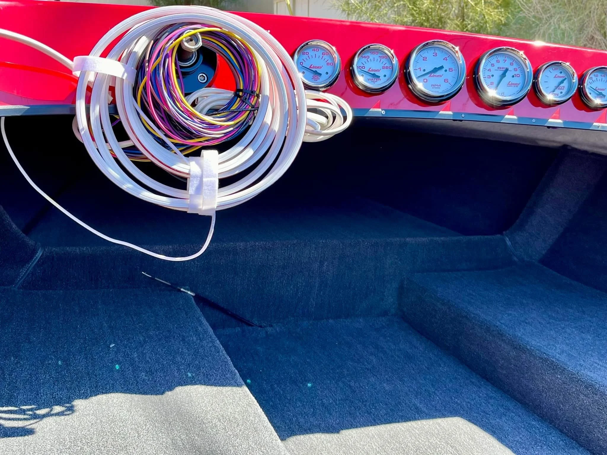 Dashboard of a boat with various gauges, and a large coil of multicolored wires resting on the dashboard.