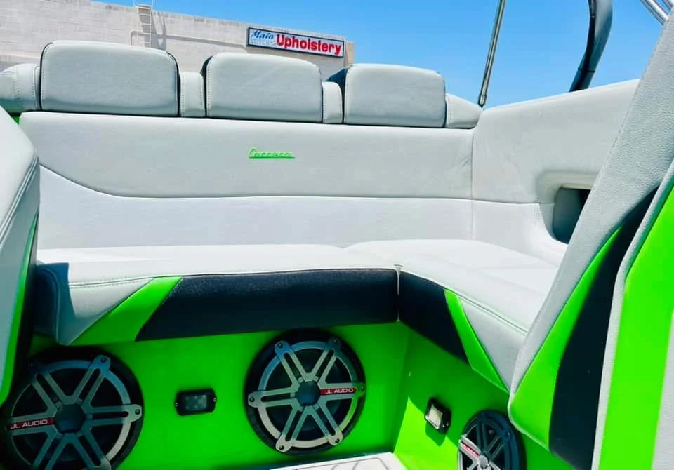 The interior of a boat featuring white cushioned seating with green and black accents and multiple speakers.