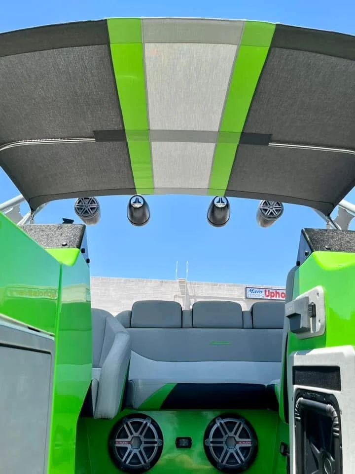 The interior view of a boat or yacht, featuring a seating area with grey and green accents, multiple speakers, and a canopy or sunshade with green and grey sections.