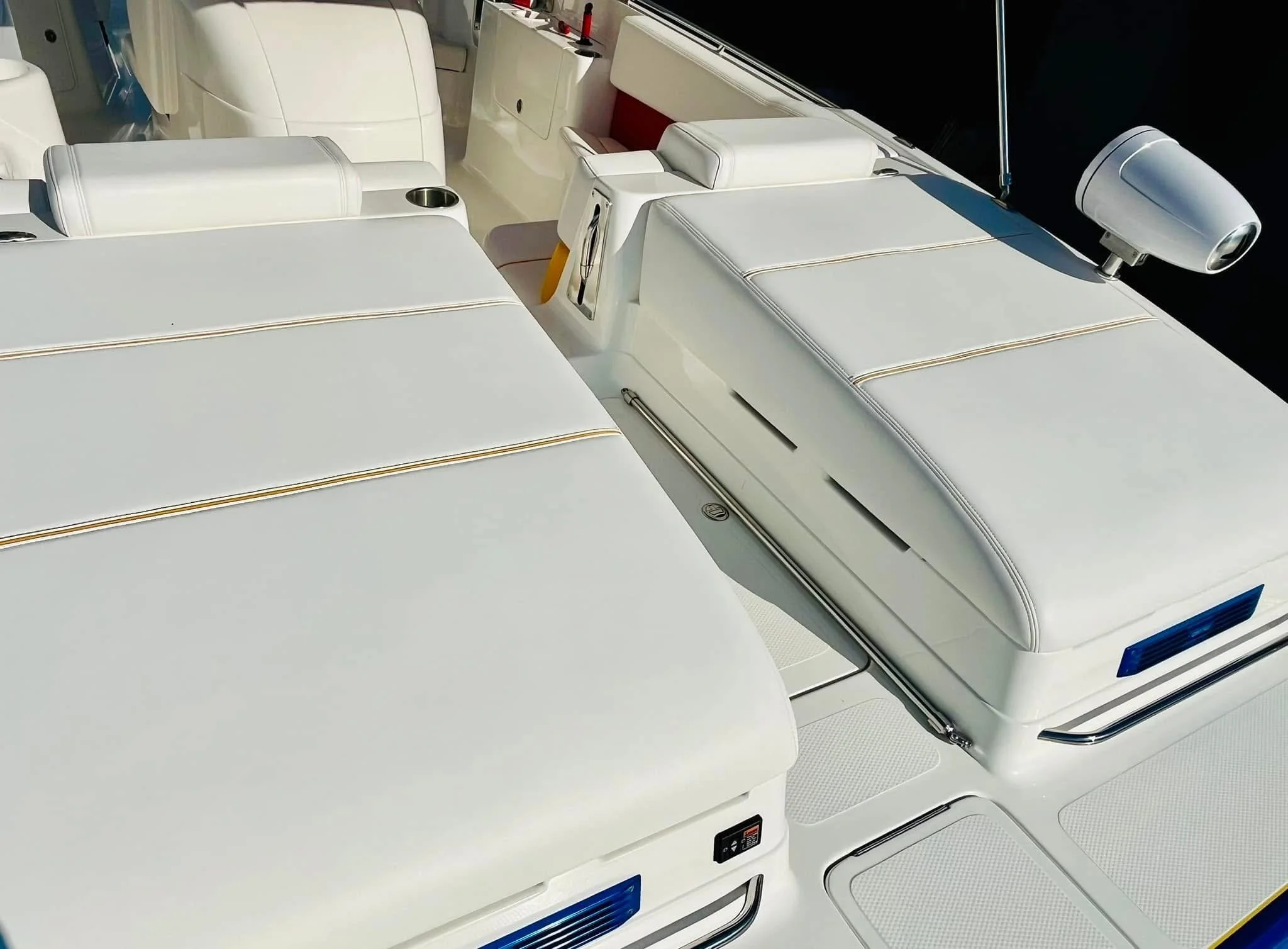Close-up of a white yacht's deck showing cushioned seating, a mounted spotlight, and various compartments.