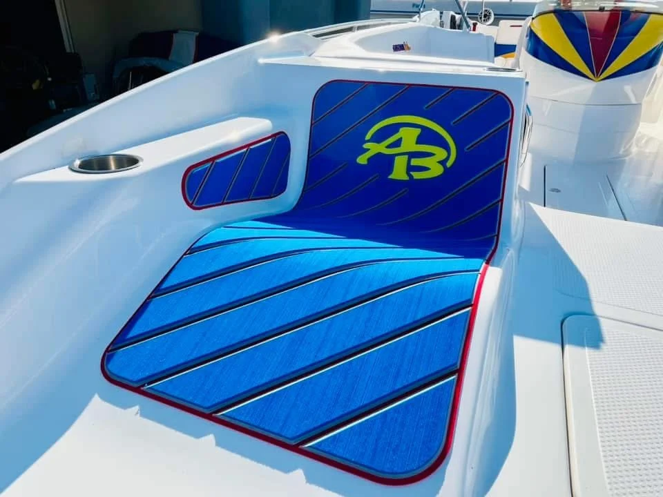 Close-up of a boat seat with blue cushion and a logo, surrounded by white fiberglass, with a drink holder nearby.
