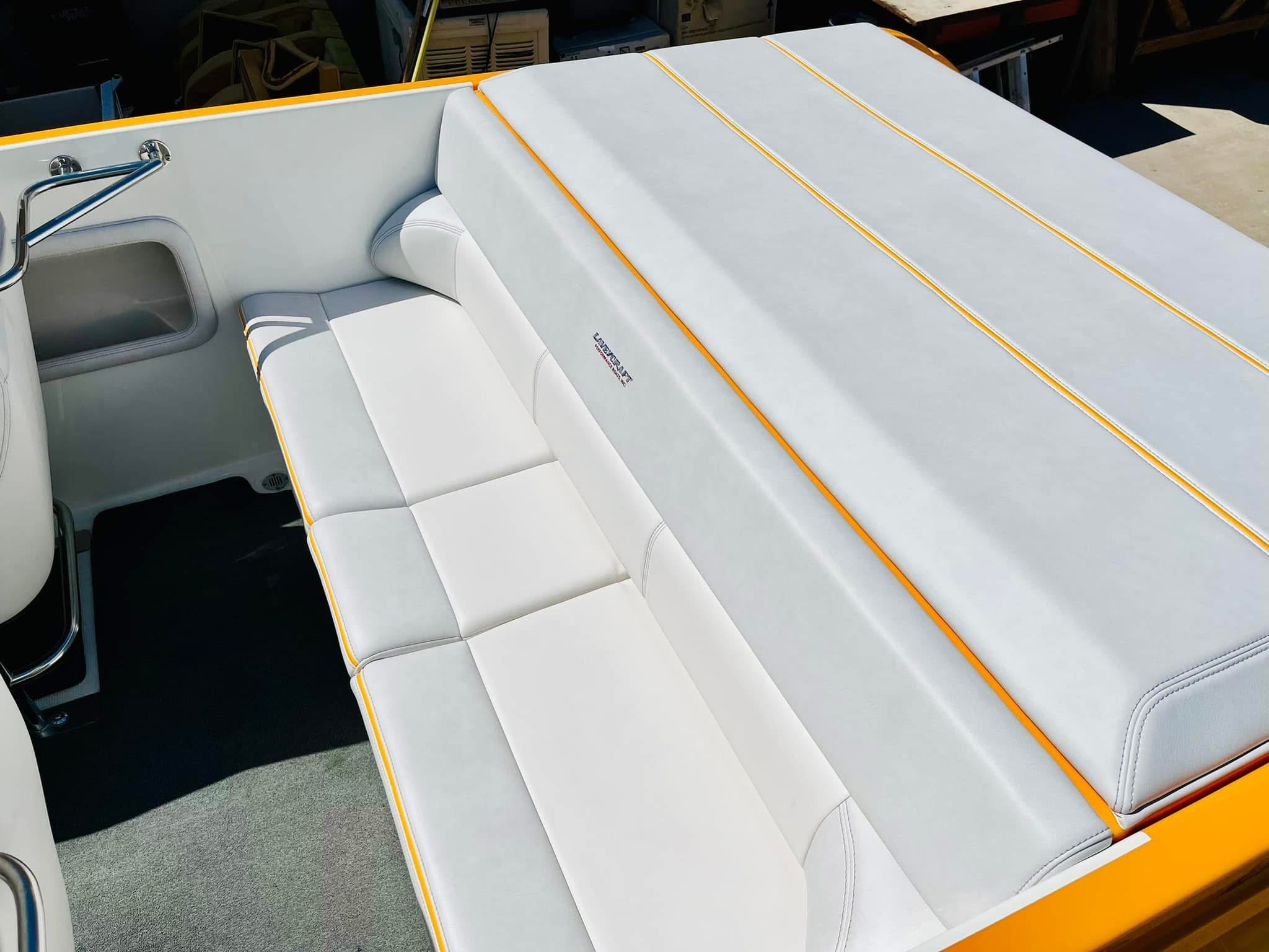 Close-up of a white boat bench seat with yellow piping, part of a boat interior with metal handlebar and black flooring.