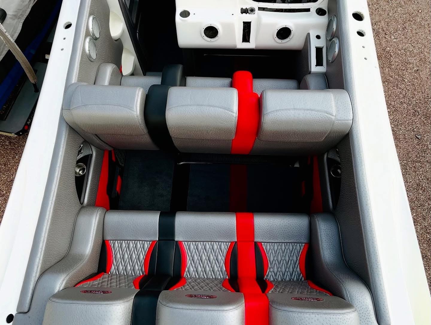 Interior of a boat showing multiple fitted seats with grey, black, and red upholstery, and audio speakers built into the walls.