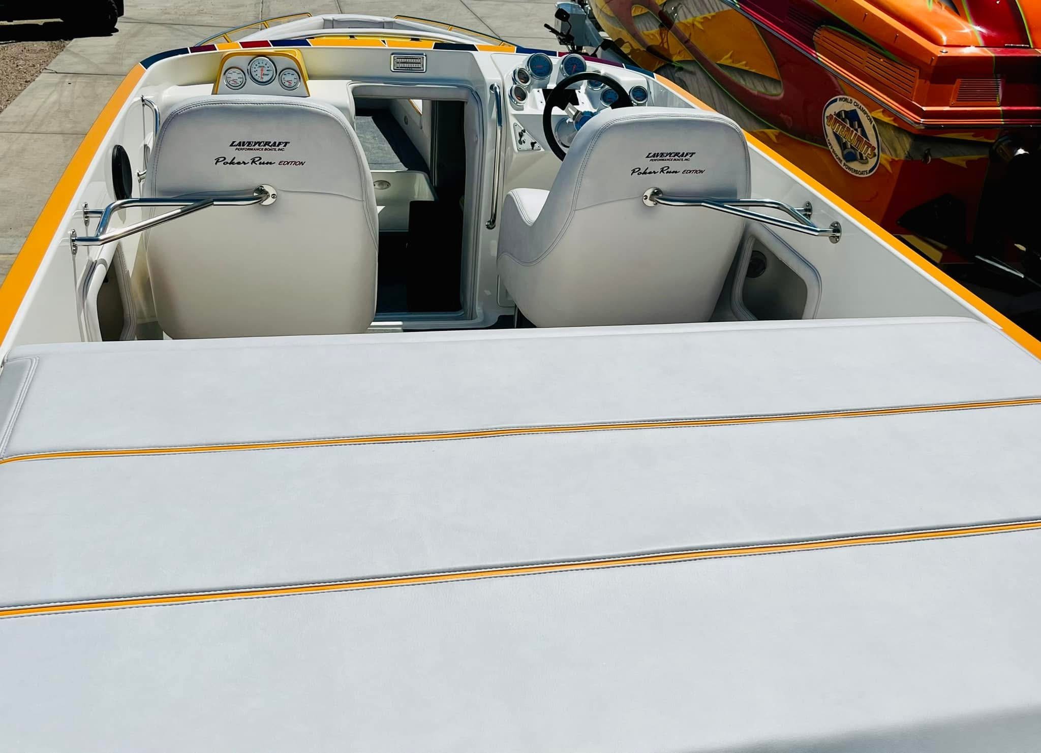 Interior of a vintage speedboat with white seats and a dashboard with gauges, parked next to a colorful boat with racing decals.