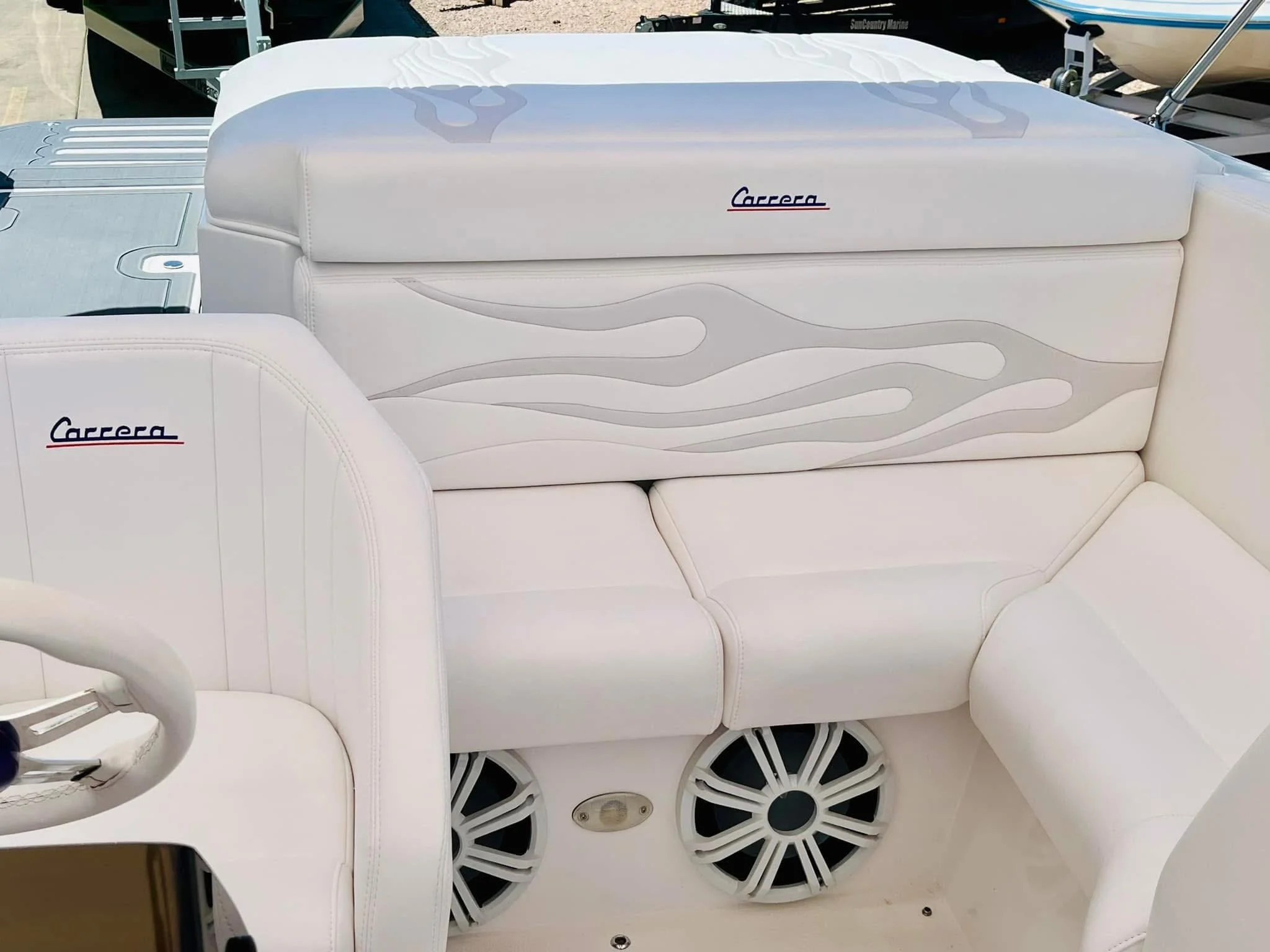 White leather seating area on a boat with 'Carrera' embroidered on the cushions, and large speakers integrated into the floor.