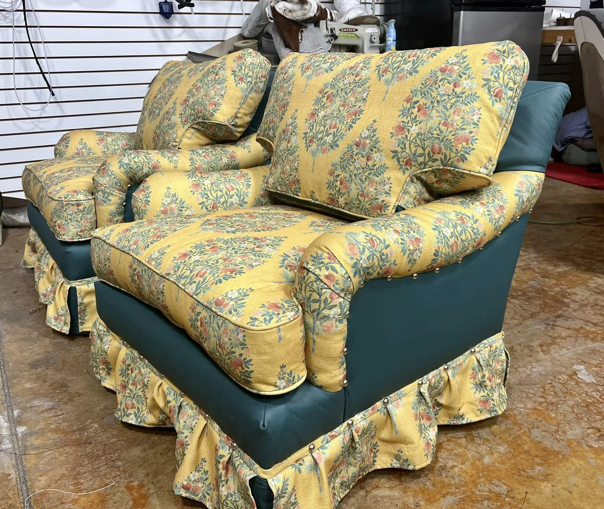 A floral patterned yellow and blue upholstered couch with matching cushions, seen in a cluttered room with a wooden floor and various objects in the background.