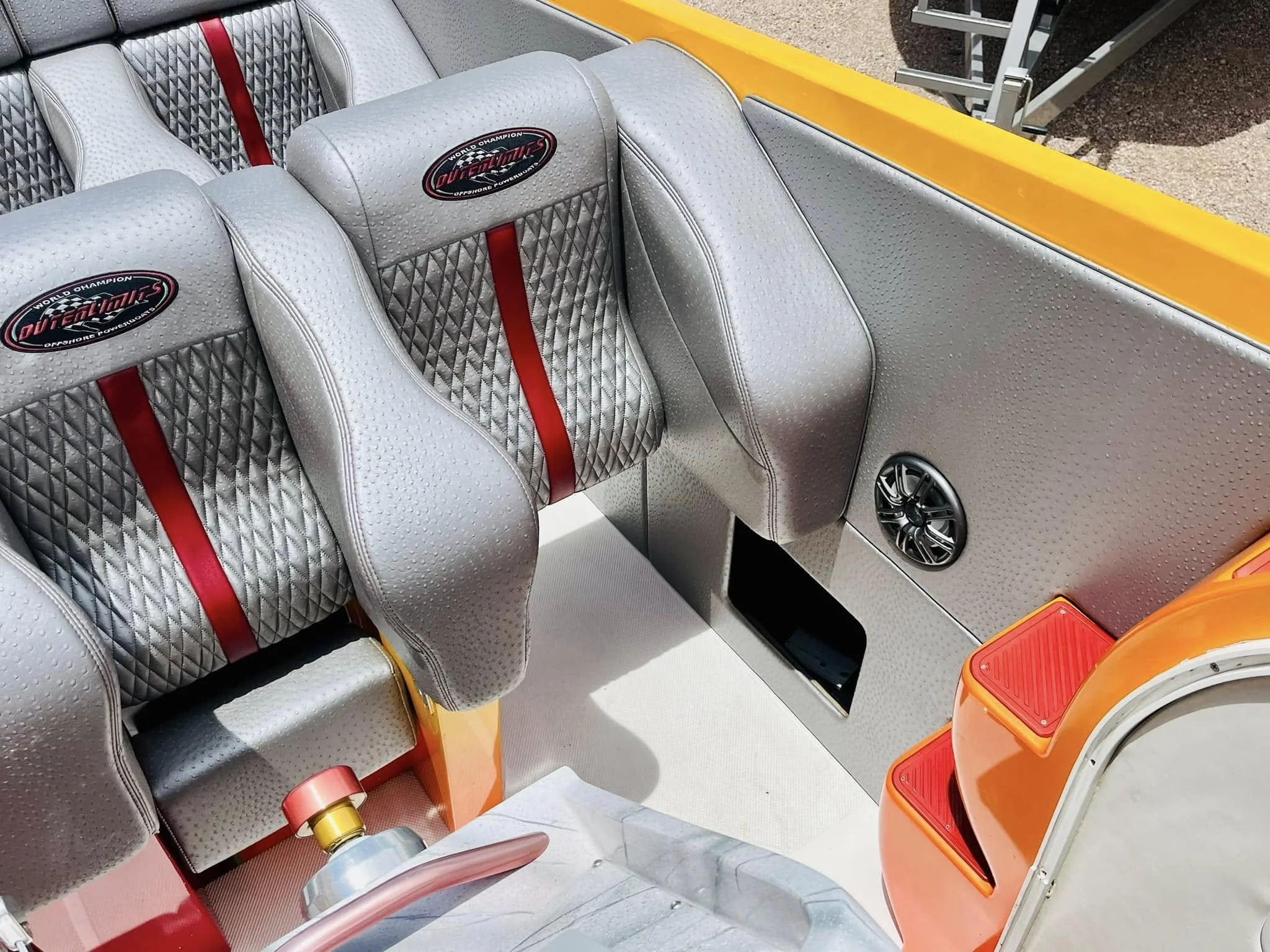 Interior of a boat with gray and red quilted seats, a speaker, and orange steps.
