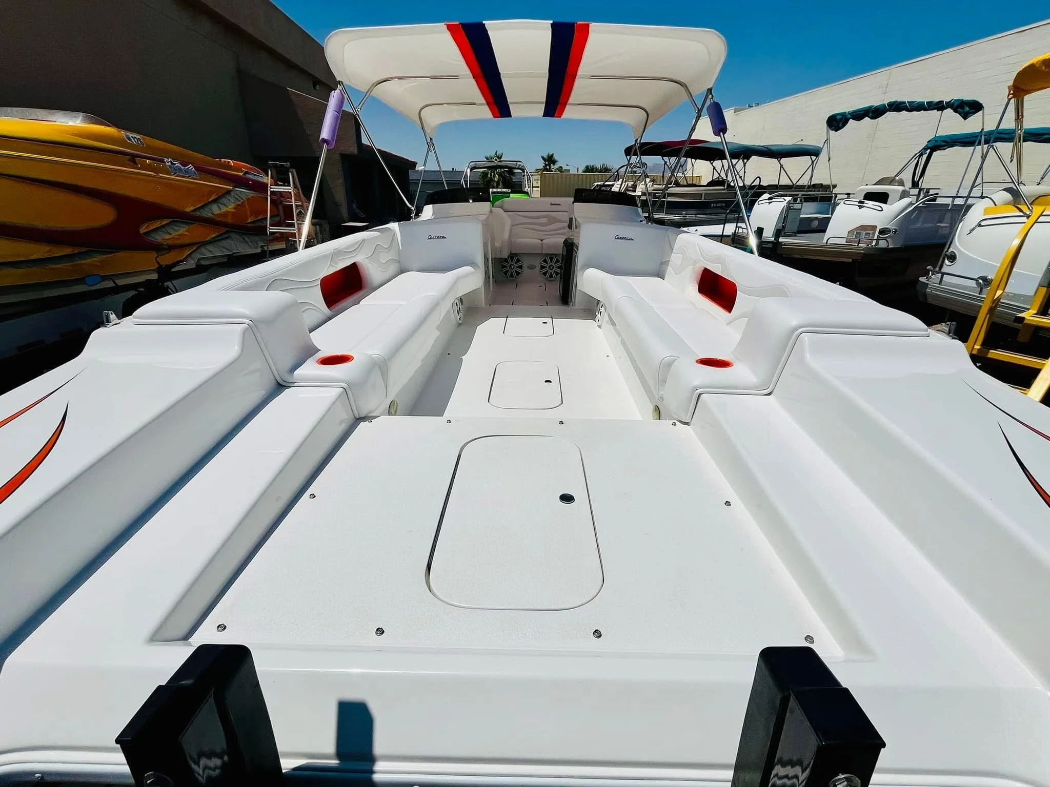 View of the deck of a white pontoon boat with built-in seating, cup holders, and a canopy, surrounded by other boats at a marina.